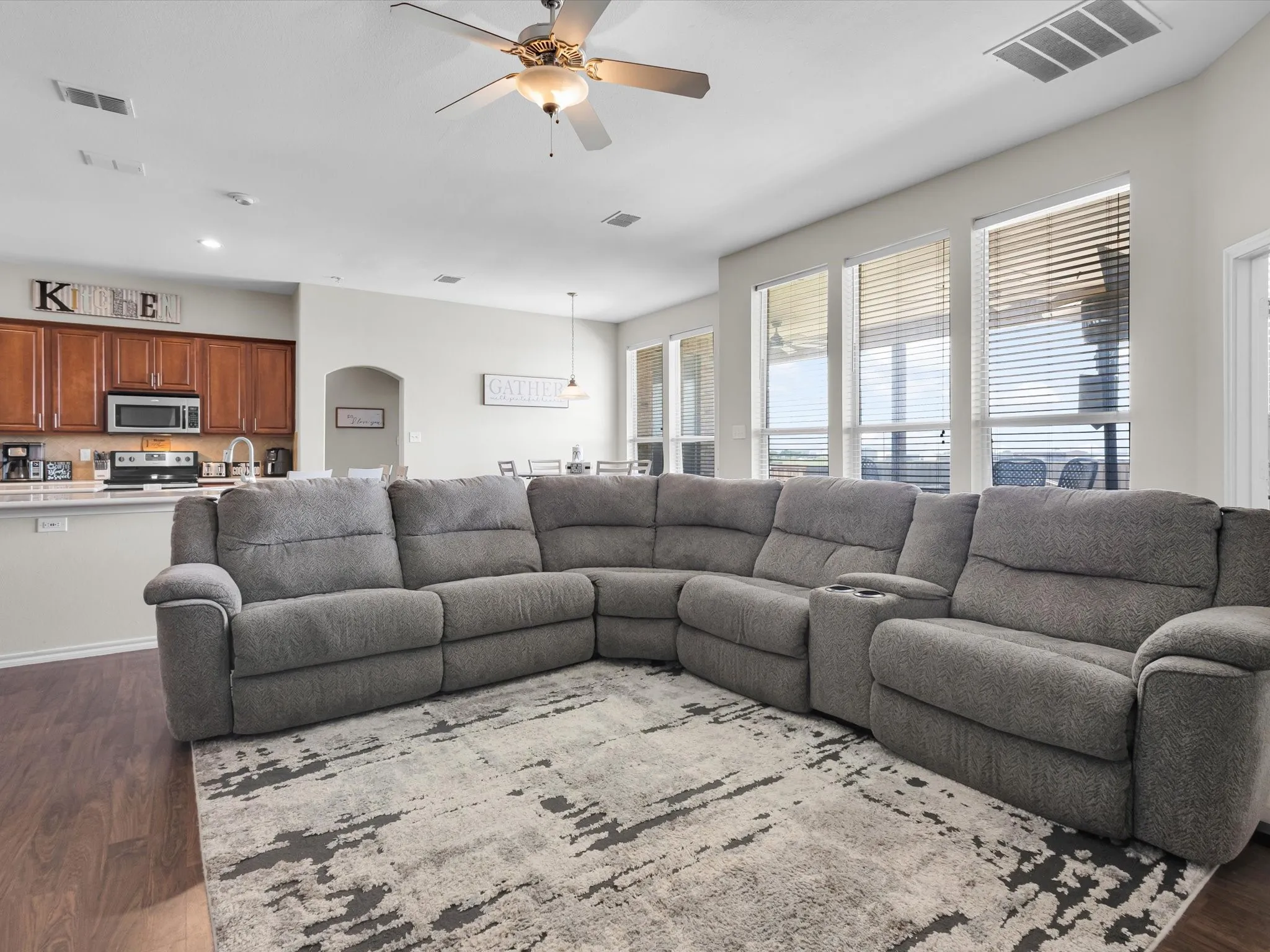 Expansive living area featuring wood-finish flooring, a ceiling fan, and multiple windows with blinds