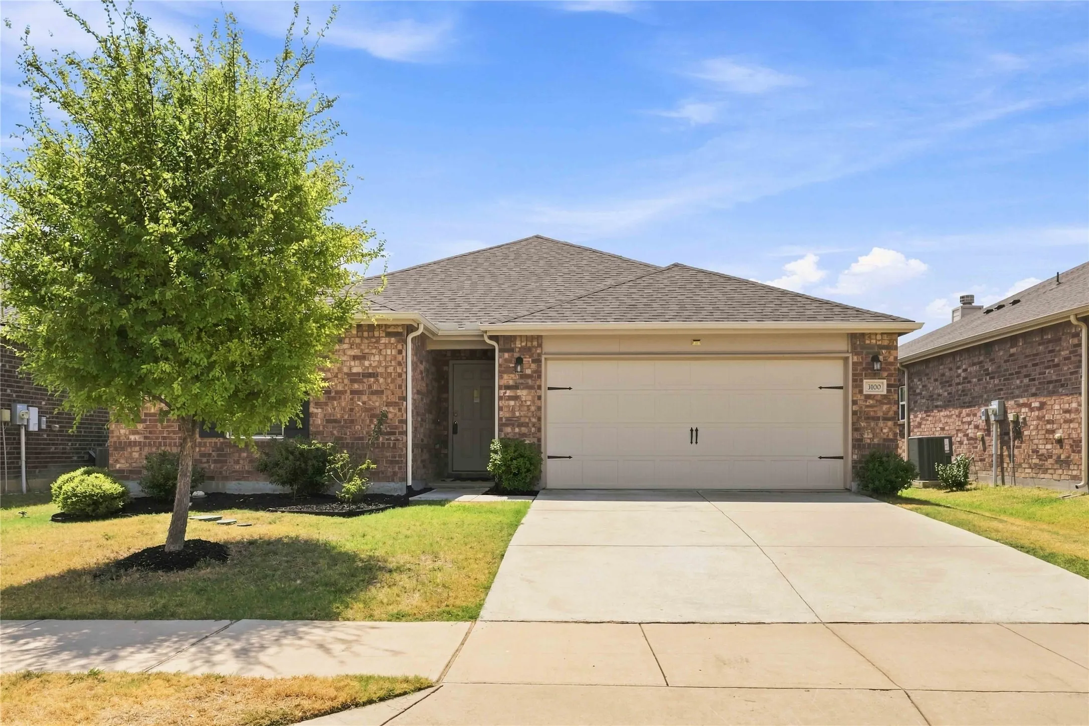Brick exterior with a shingled roof, two-car garage, concrete driveway, and front yard landscaping