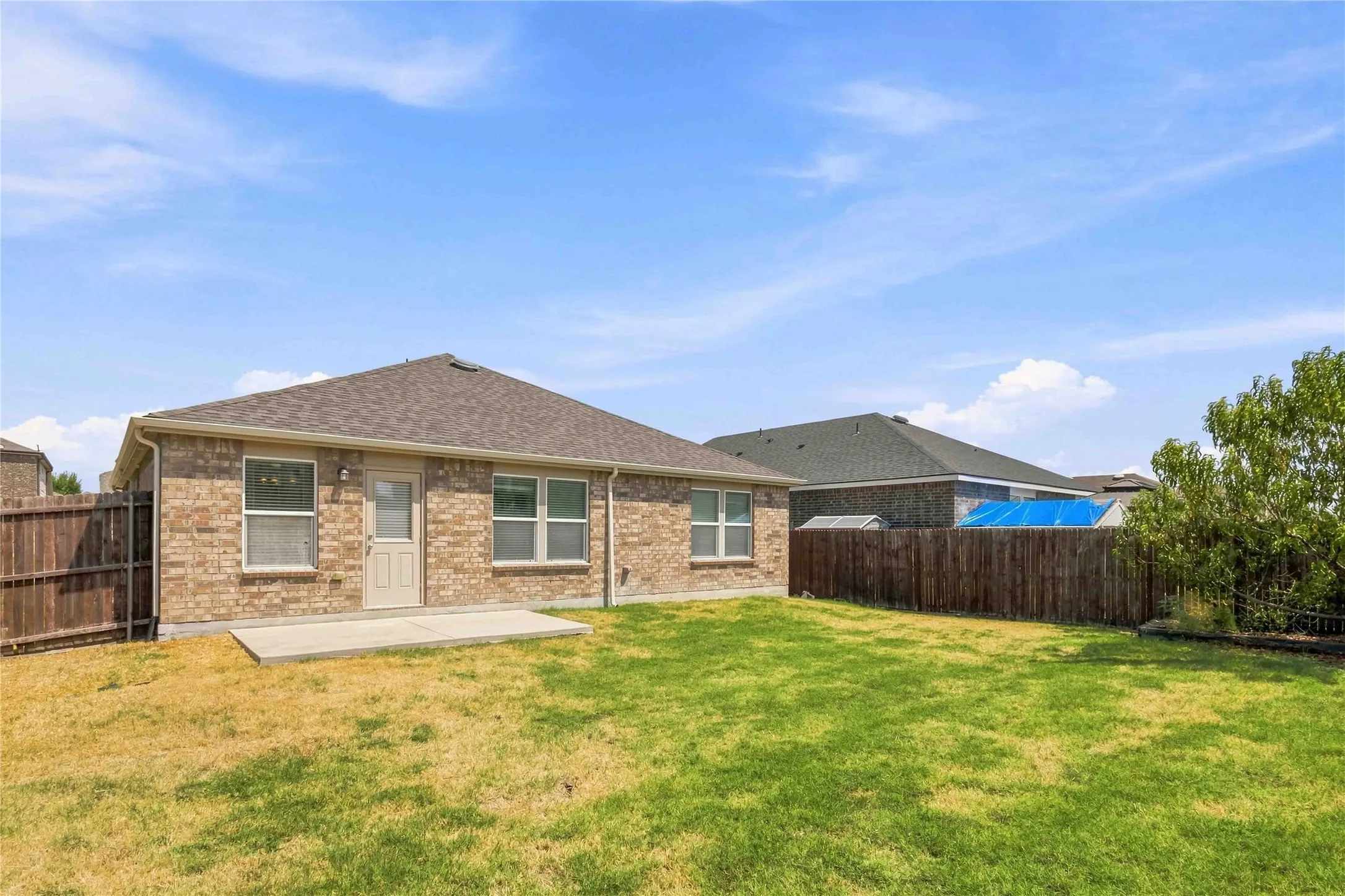 Expansive backyard with a manicured lawn, full privacy fencing, and a concrete patio