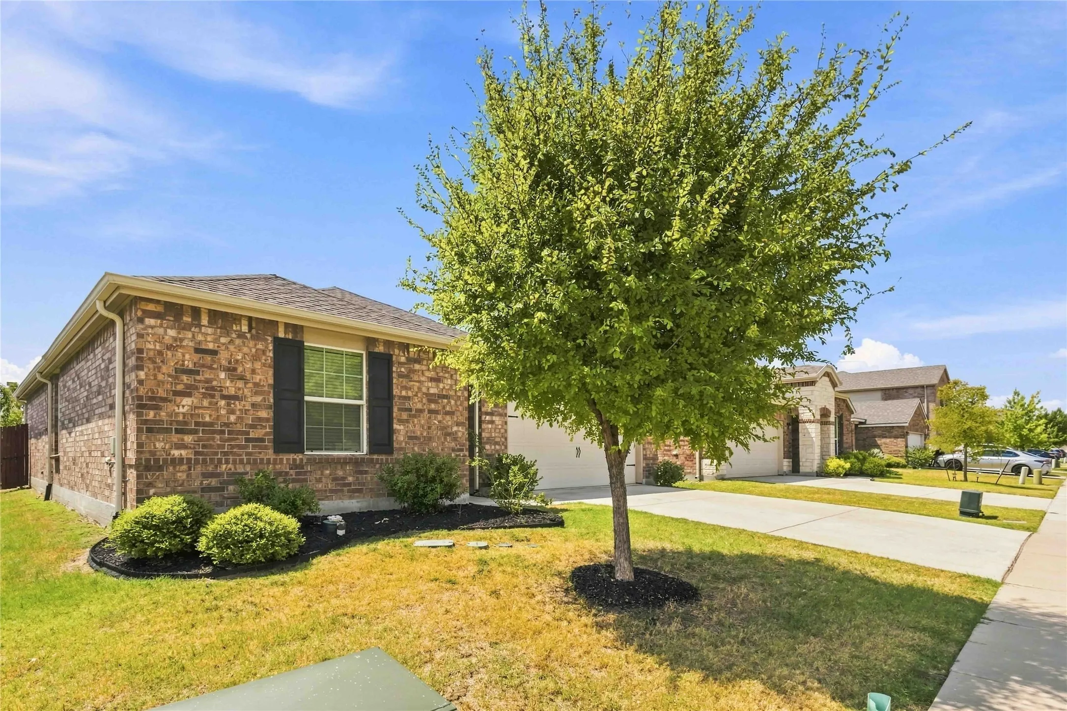 Brick exterior with dark shutters, front landscaping, mature tree, and concrete driveway