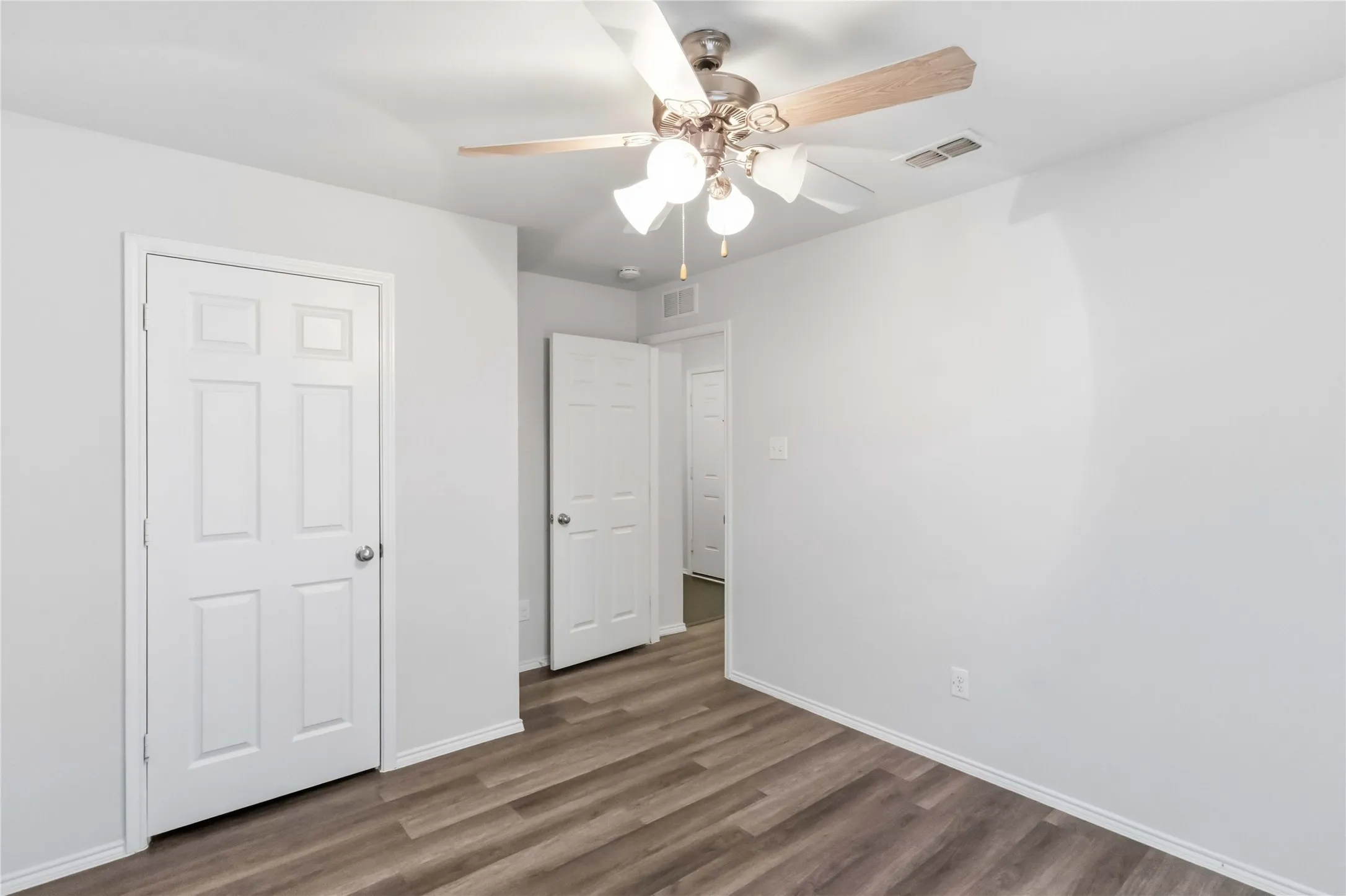Wood-finish flooring, ceiling fan with light fixture, white interior doors, and neutral wall paint