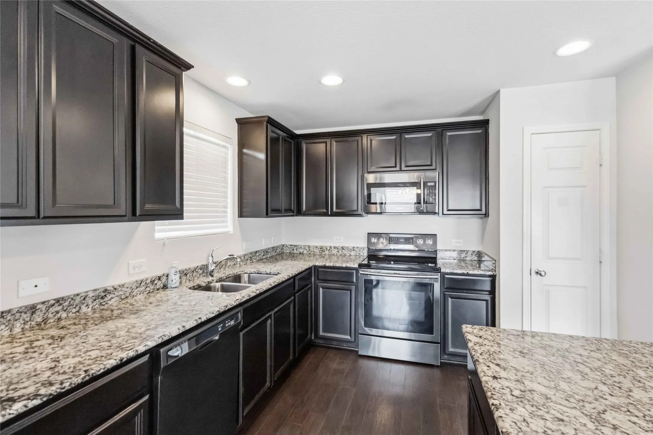 Kitchen featuring dark wood-finish cabinetry, light-toned countertops, stainless steel appliances, a dual basin sink, and recessed lighting