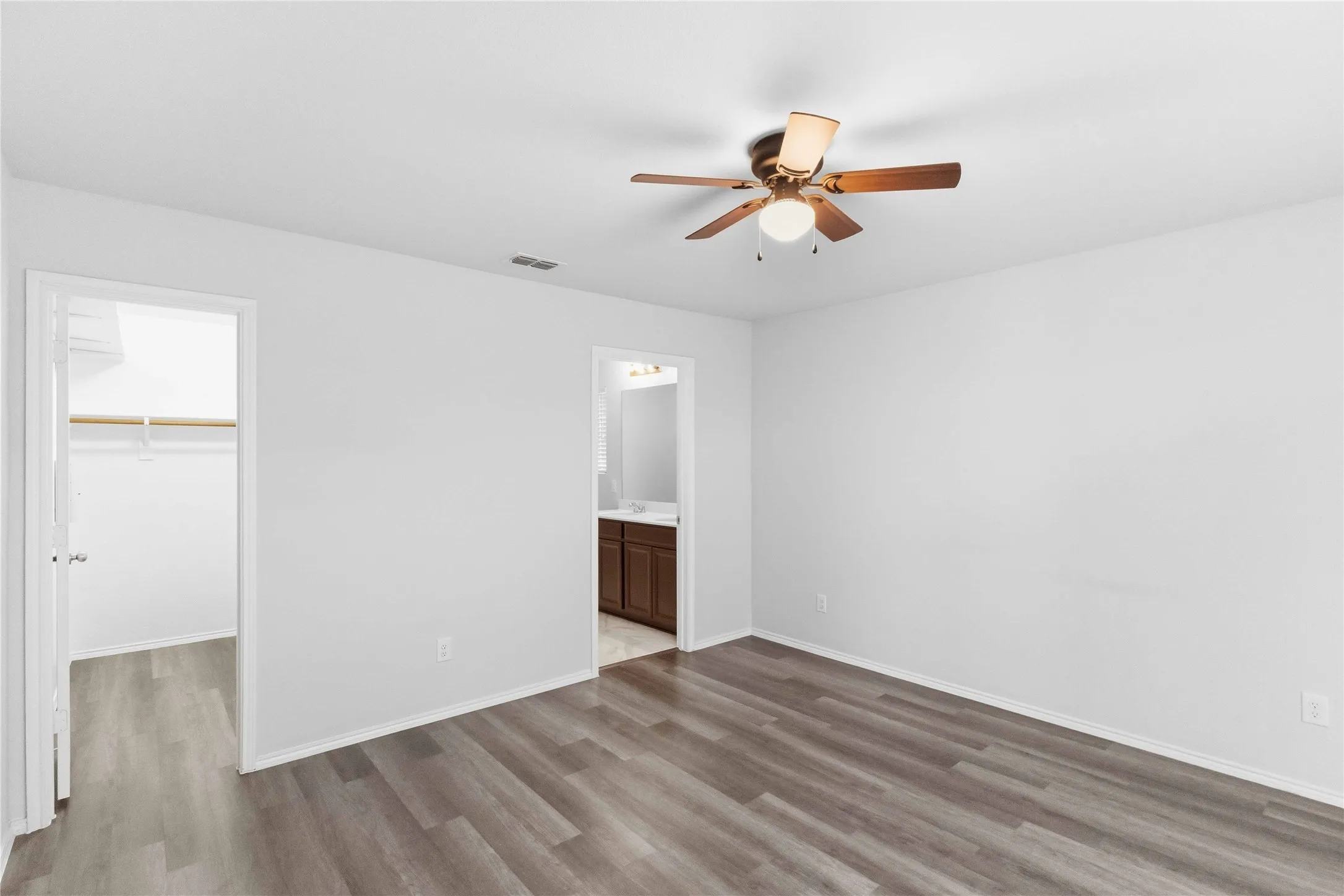 Wood-finish flooring with crisp white walls, a ceiling fan with integrated lighting, and a walk-in closet with built-in shelving