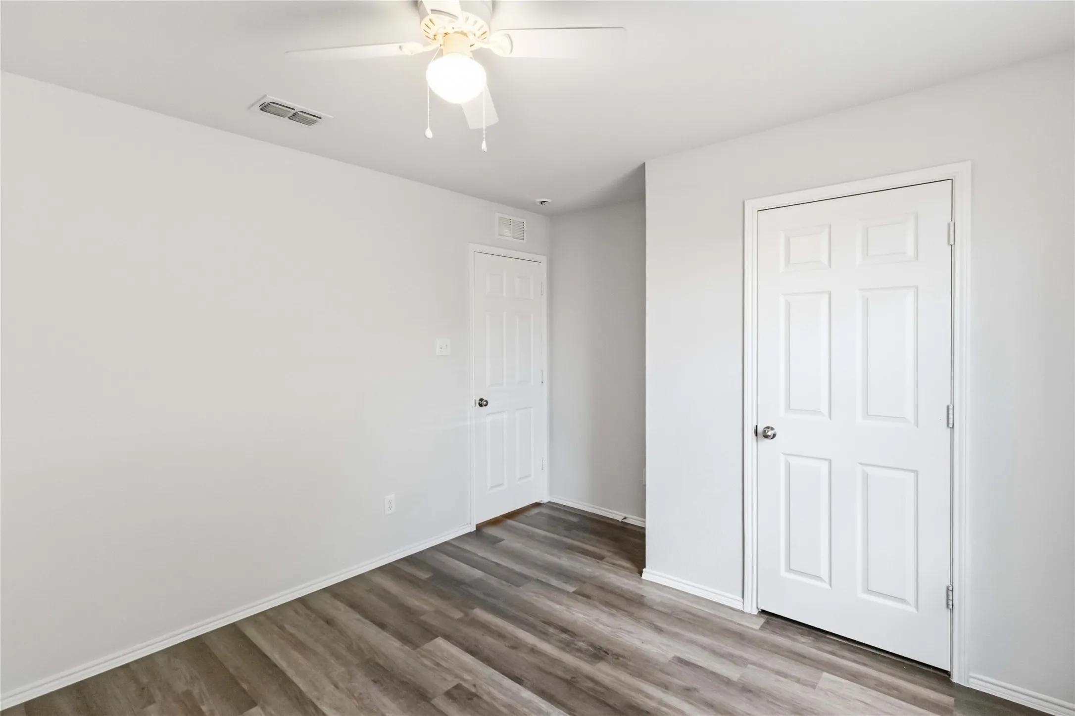 Wood-finish flooring, white paneled doors, and a ceiling fan with integrated lighting
