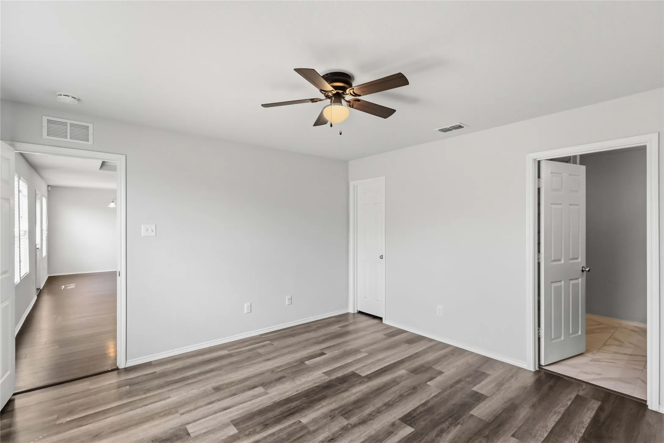 Wood-finish flooring, ceiling fan with light fixture, and white painted walls