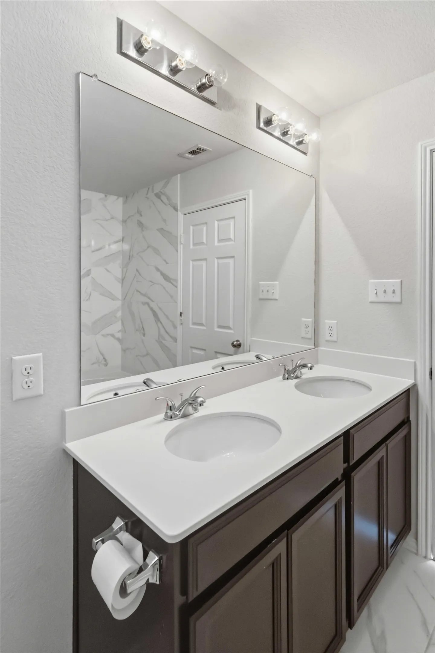Dual vanity with a white countertop and integrated sinks, brushed nickel faucets, and dark wood-finish cabinetry
