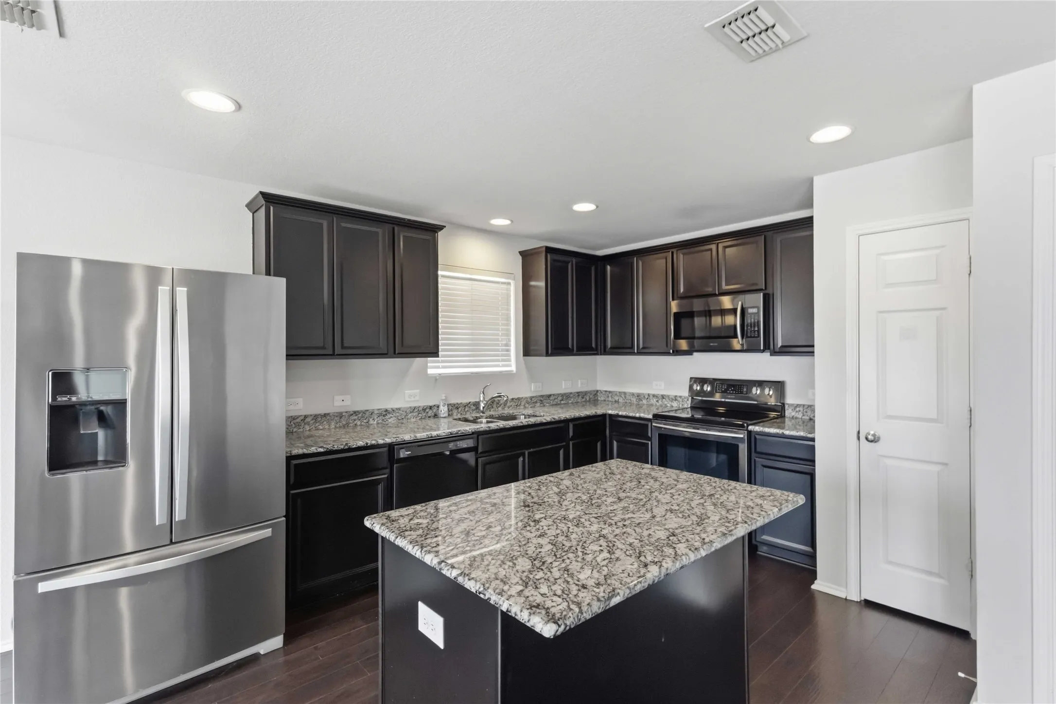 Kitchen featuring dark wood-finish cabinetry, stainless steel appliances, a center island, and granite countertops