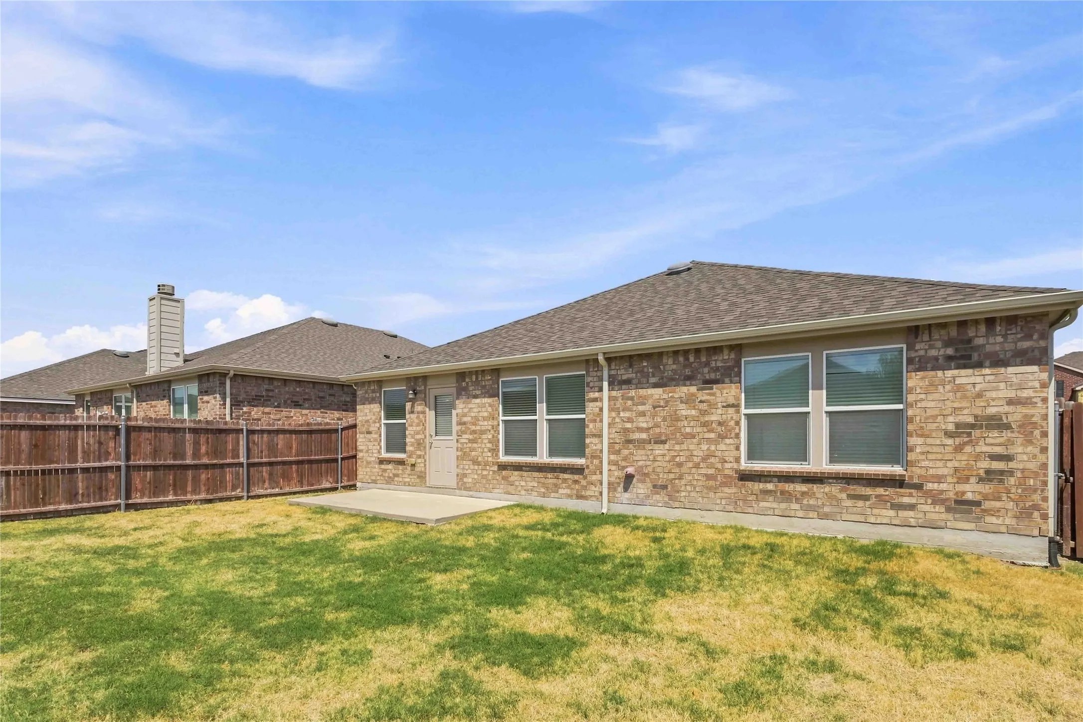 Exterior brick siding, concrete patio, double-pane windows, and a wood-panel fence