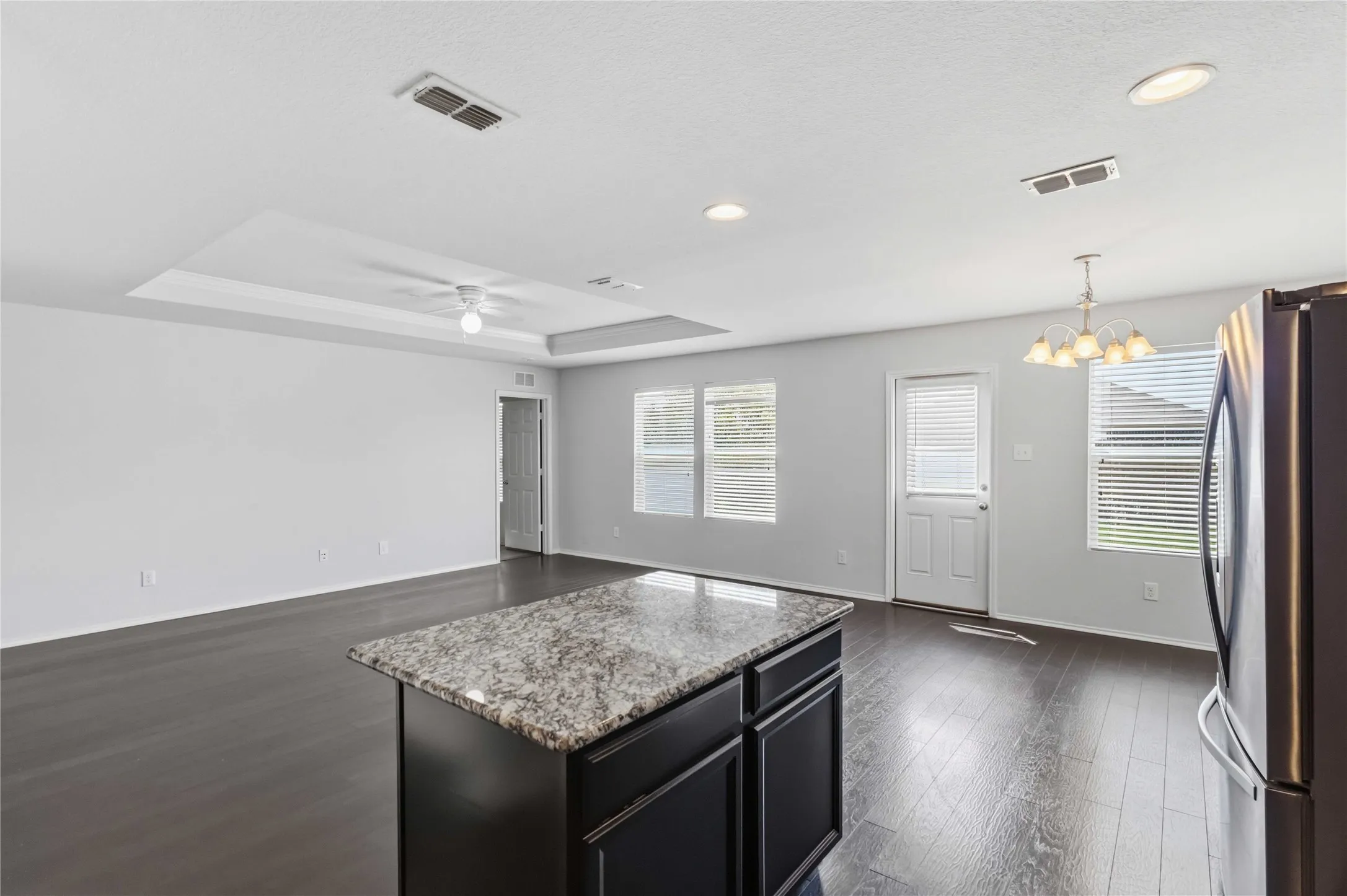 Open-concept living space featuring wood-finish flooring, a kitchen island with stone countertop, recessed lighting, and a tray ceiling with a ceiling fan