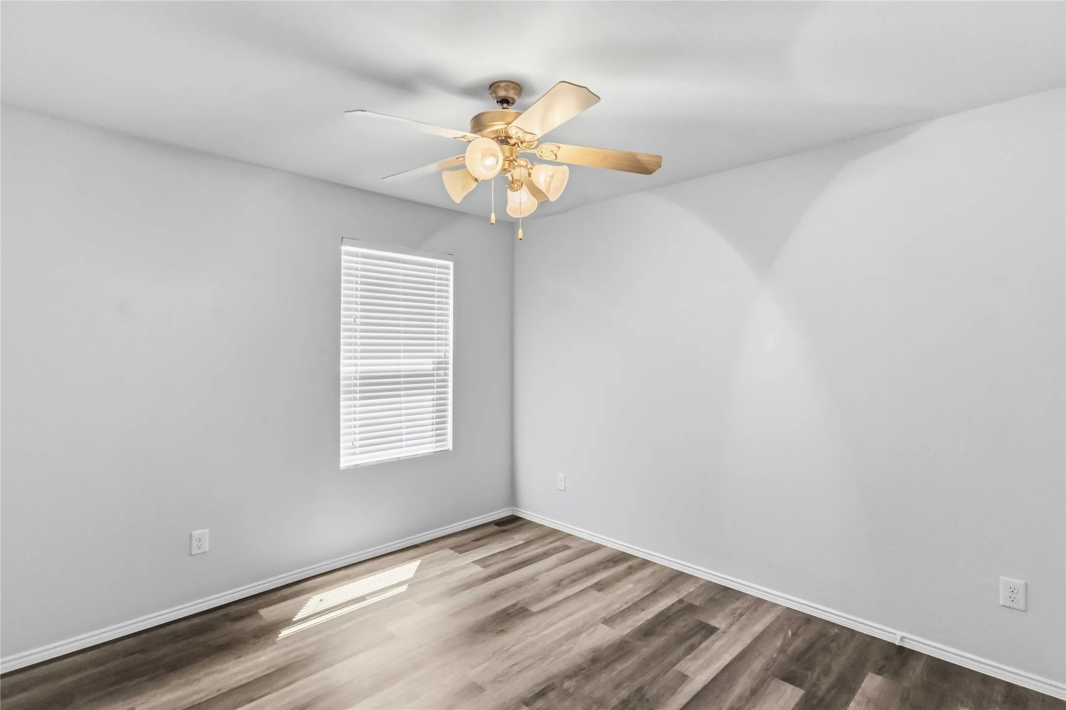 Room featuring light gray walls, wood-finish flooring, a window with blinds, and a ceiling fan with integrated lighting