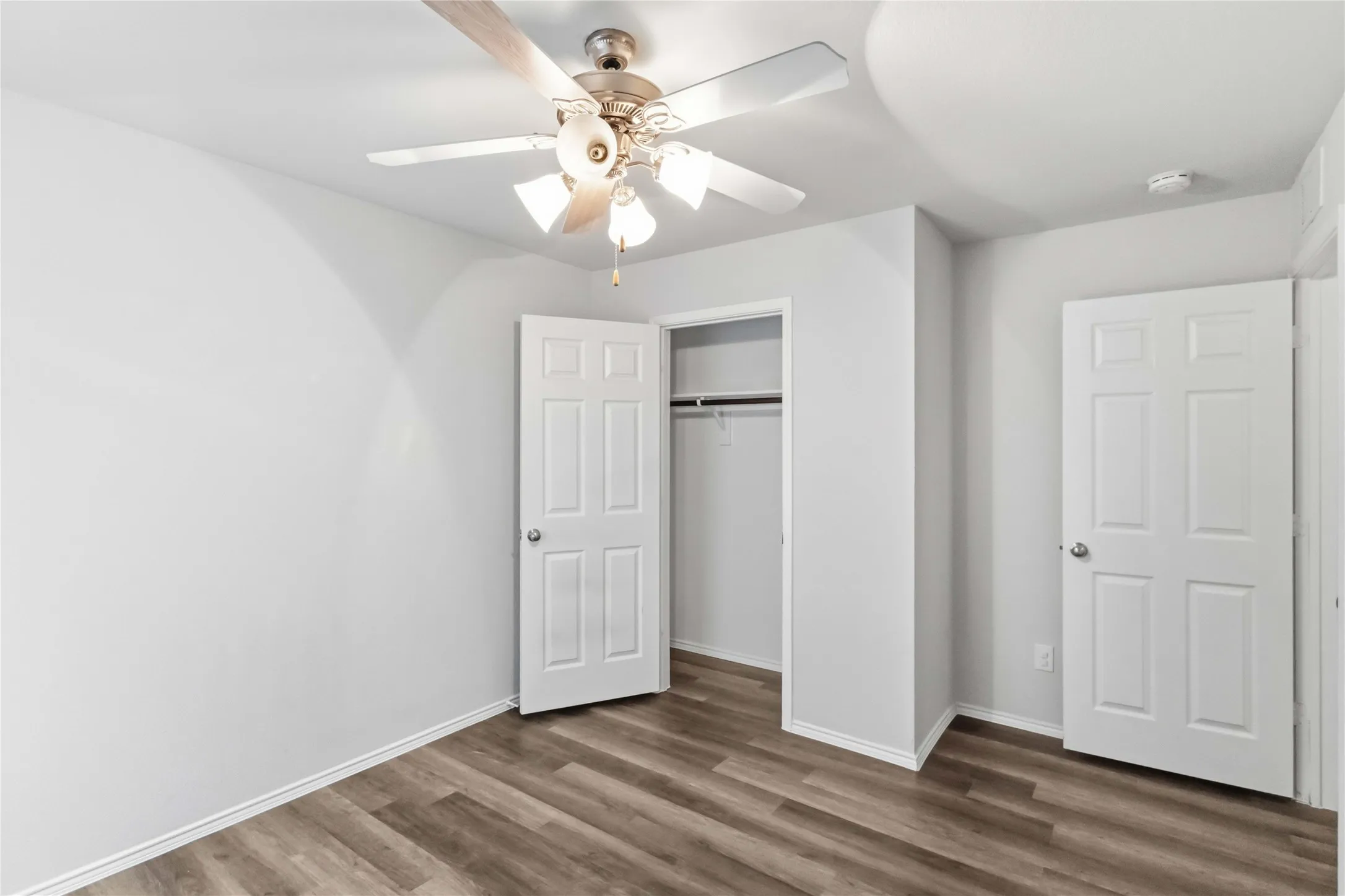 Wood-finish flooring, ceiling fan with light kit, white interior doors, and a built-in closet with hanging rod