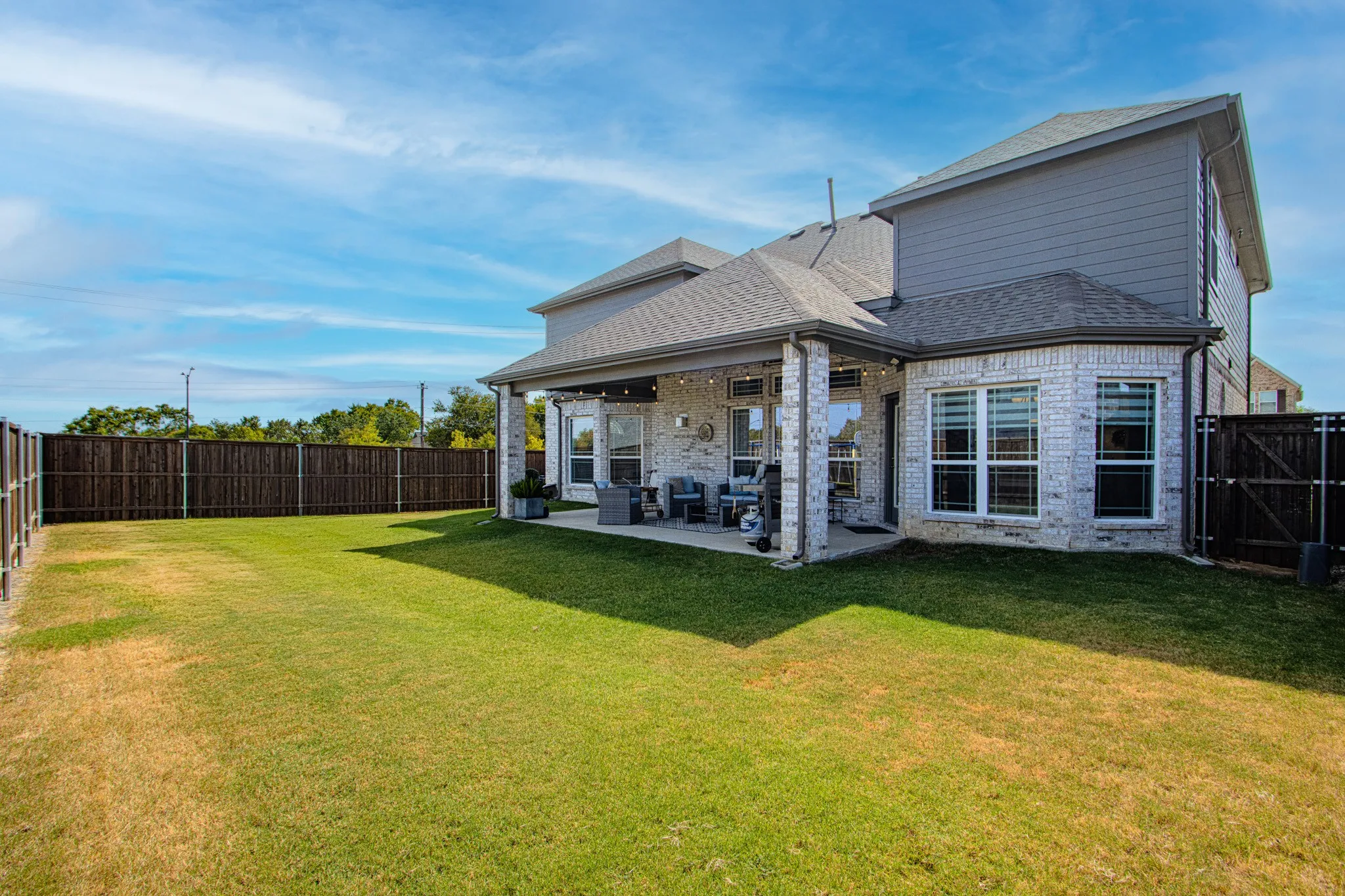 Expansive backyard featuring a manicured lawn, full privacy fencing, and a covered patio with string lighting
