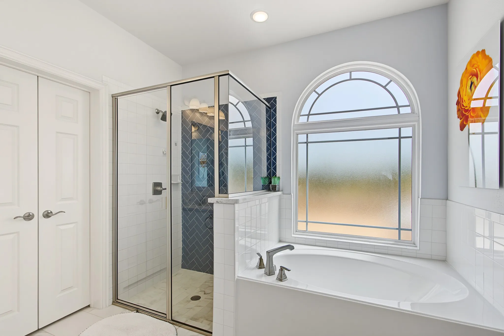 Soaking tub with brushed nickel fixtures, an arched decorative window, and a glass-enclosed shower with blue herringbone tile