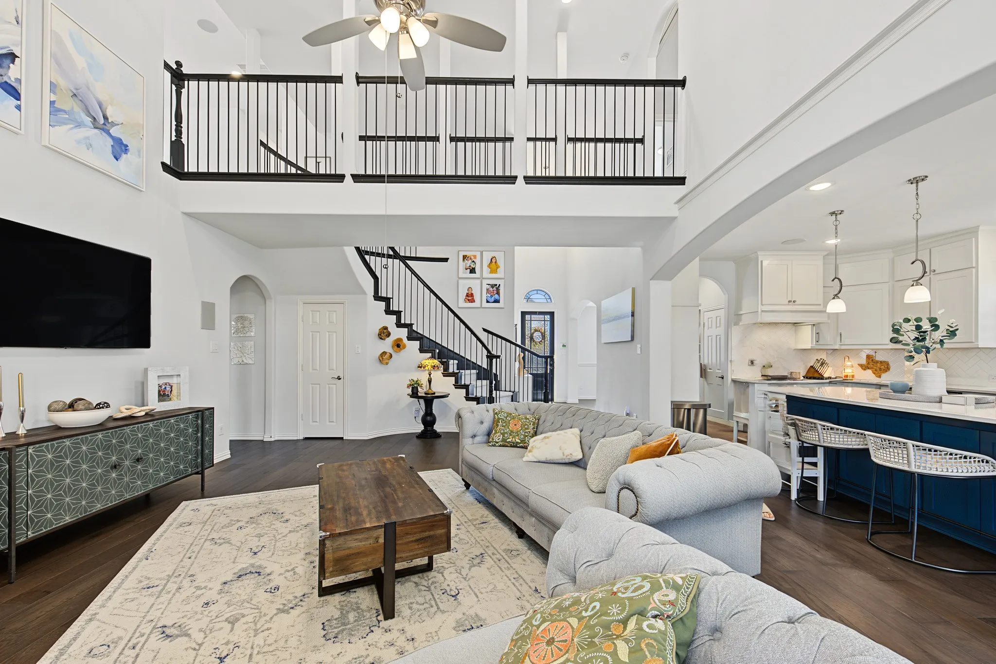 Two-story living area with dark wood-finish flooring, white walls, and a ceiling fan