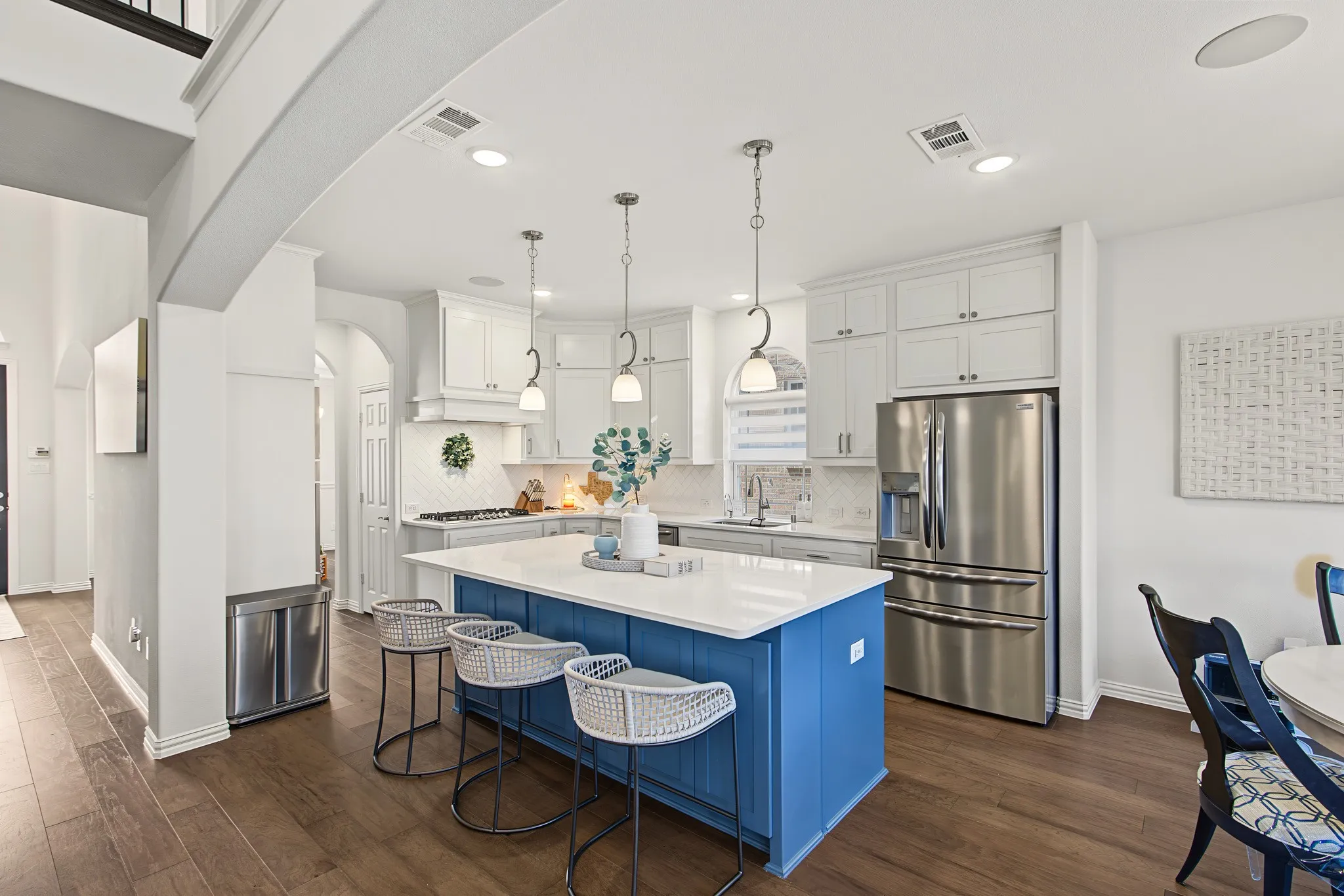 Kitchen featuring a blue-accented island with white countertop, recessed lighting, stainless steel refrigerator, white cabinetry, and wood-finish flooring