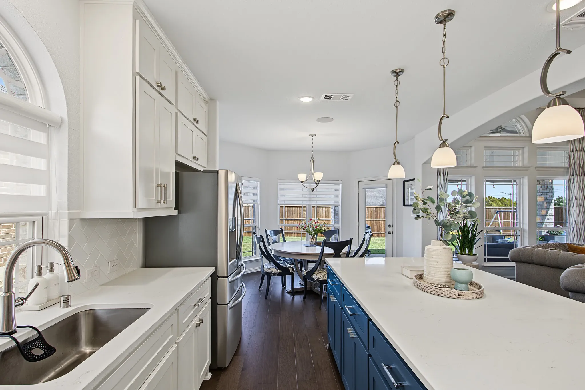 Kitchen featuring white shaker cabinetry, stainless steel sink, herringbone tile backsplash, and an expansive island with a white countertop and blue cabinetry