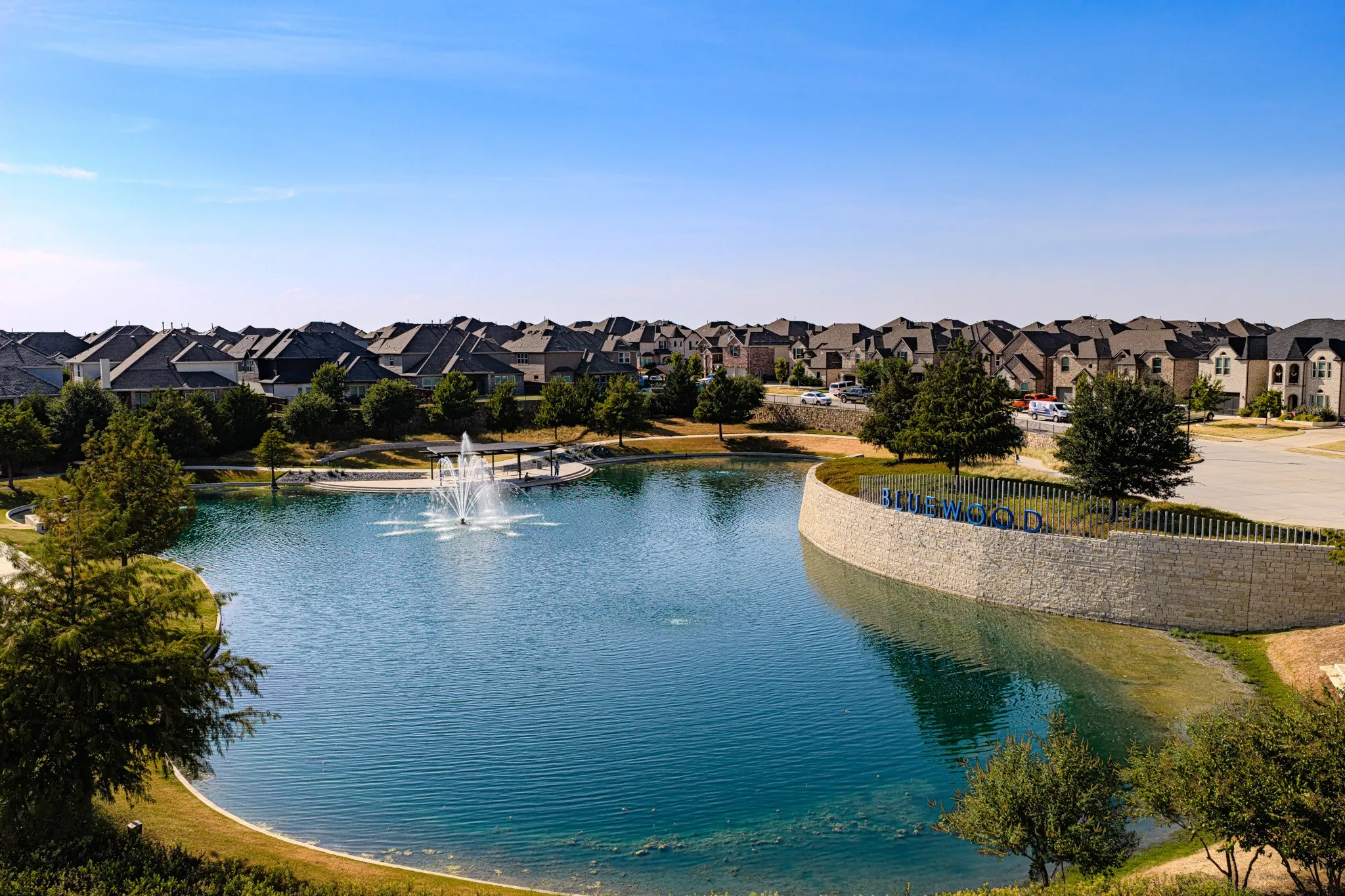 Community lake with a water feature, stone retaining wall, and mature landscaping