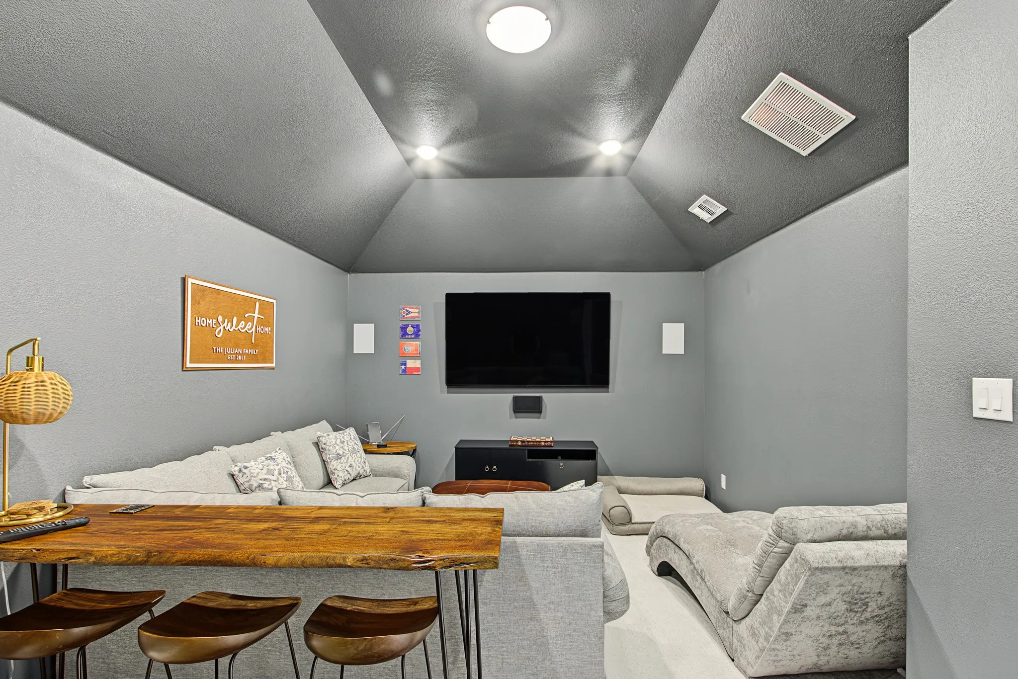 Vaulted ceiling with recessed lighting and flush-mount fixture, wall-mounted speakers, and a built-in wood-top bar with seating