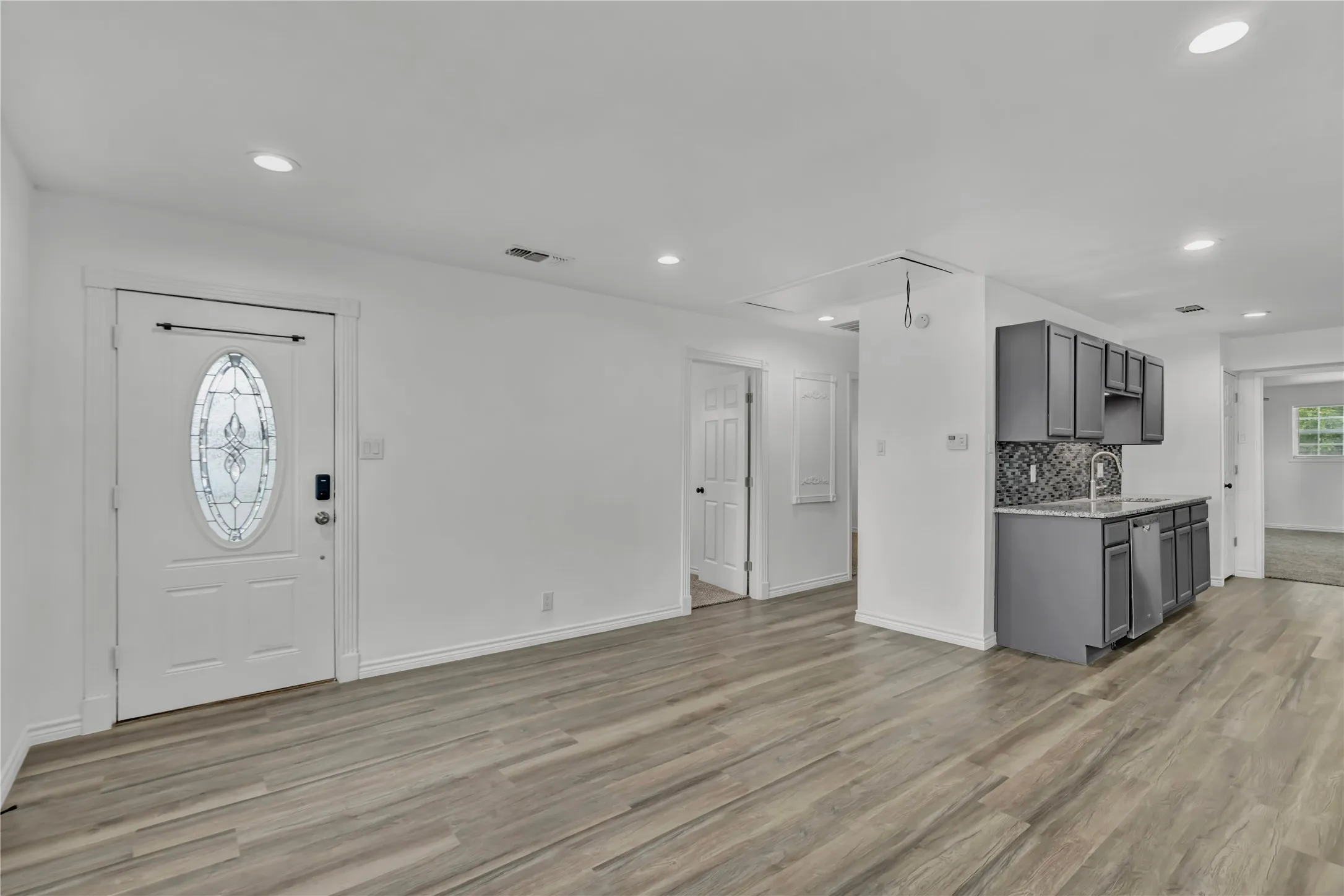 Recessed lighting, wood-finish flooring, white walls, gray cabinetry, and a mosaic tile backsplash