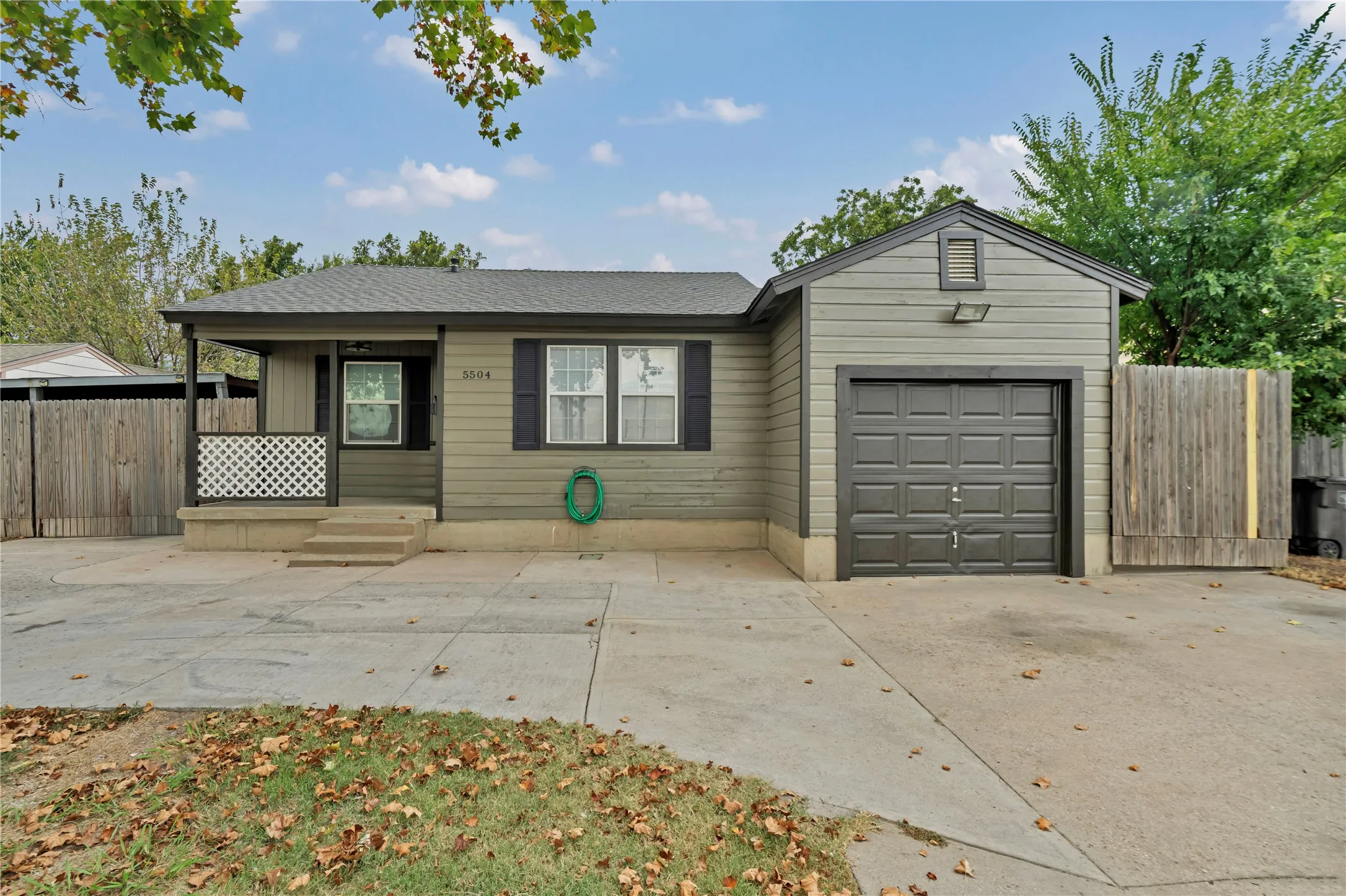 Exterior siding, attached garage, covered porch, concrete driveway, and mature trees