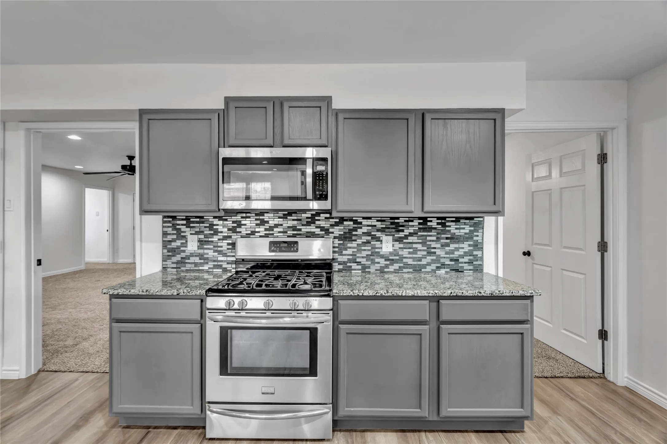 Grey cabinetry with stainless steel appliances, mosaic tile backsplash, and a light-toned countertop