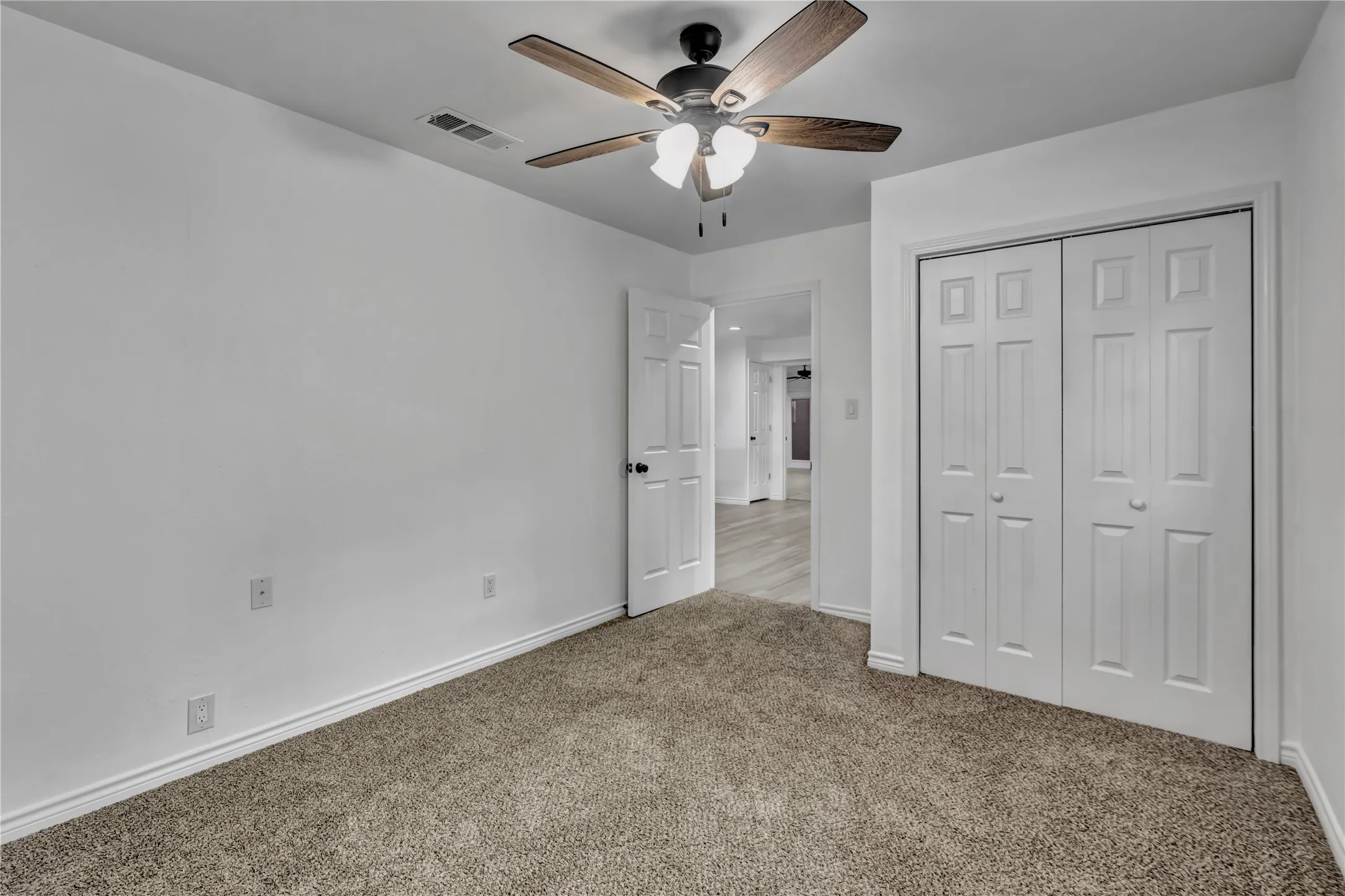 Neutral-toned carpeting, white painted walls, and a ceiling fan with light fixture