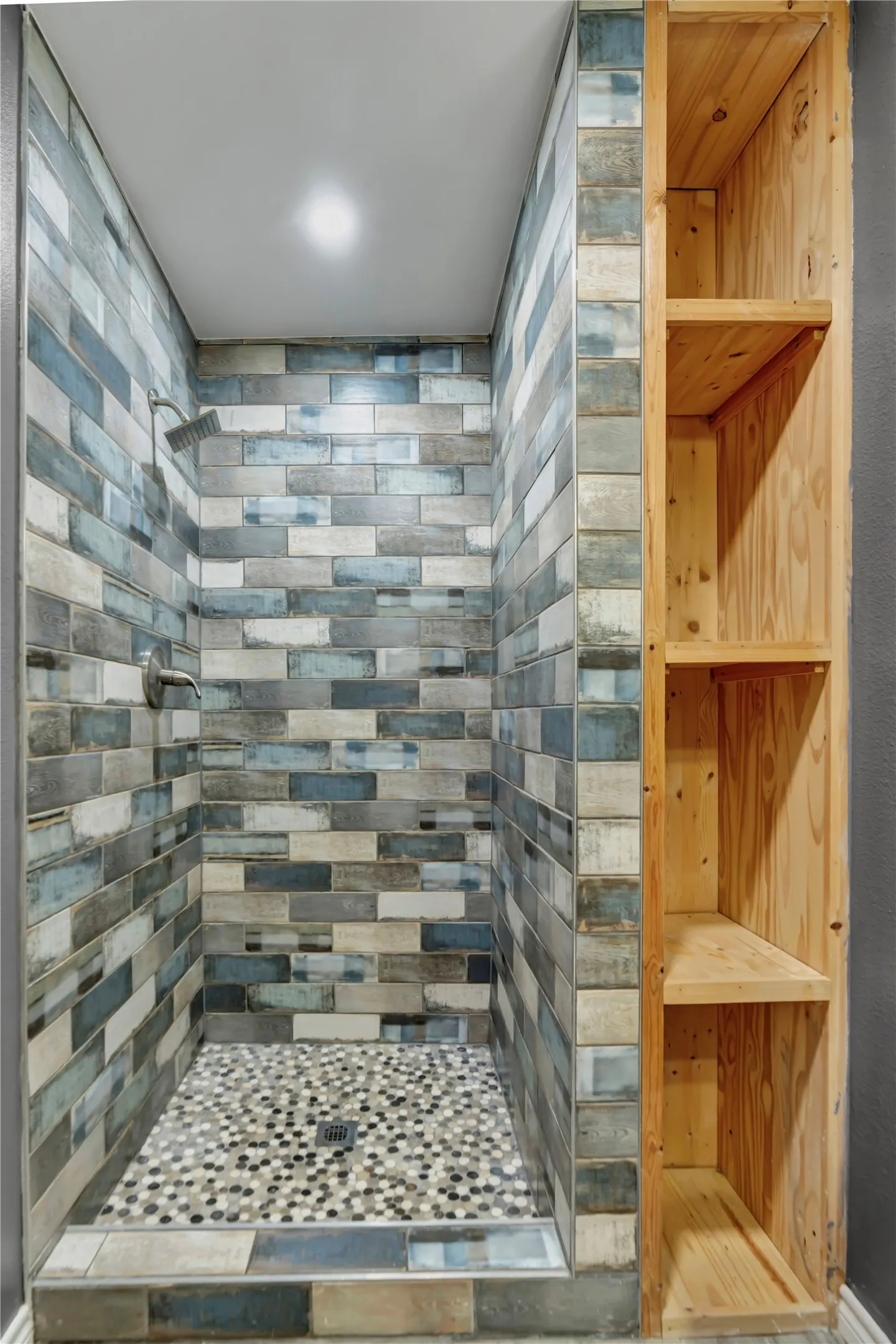Shower stall with multi-tone subway tile, mosaic tile flooring, built-in wooden shelving, and recessed lighting