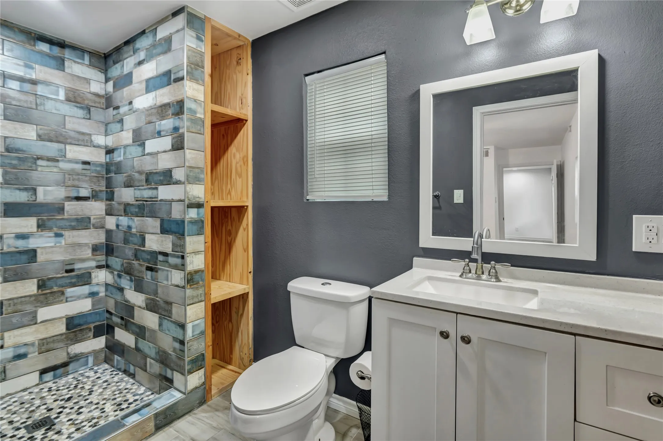 Walk-in shower with multicolor tile surround, pebble floor, and glass enclosure