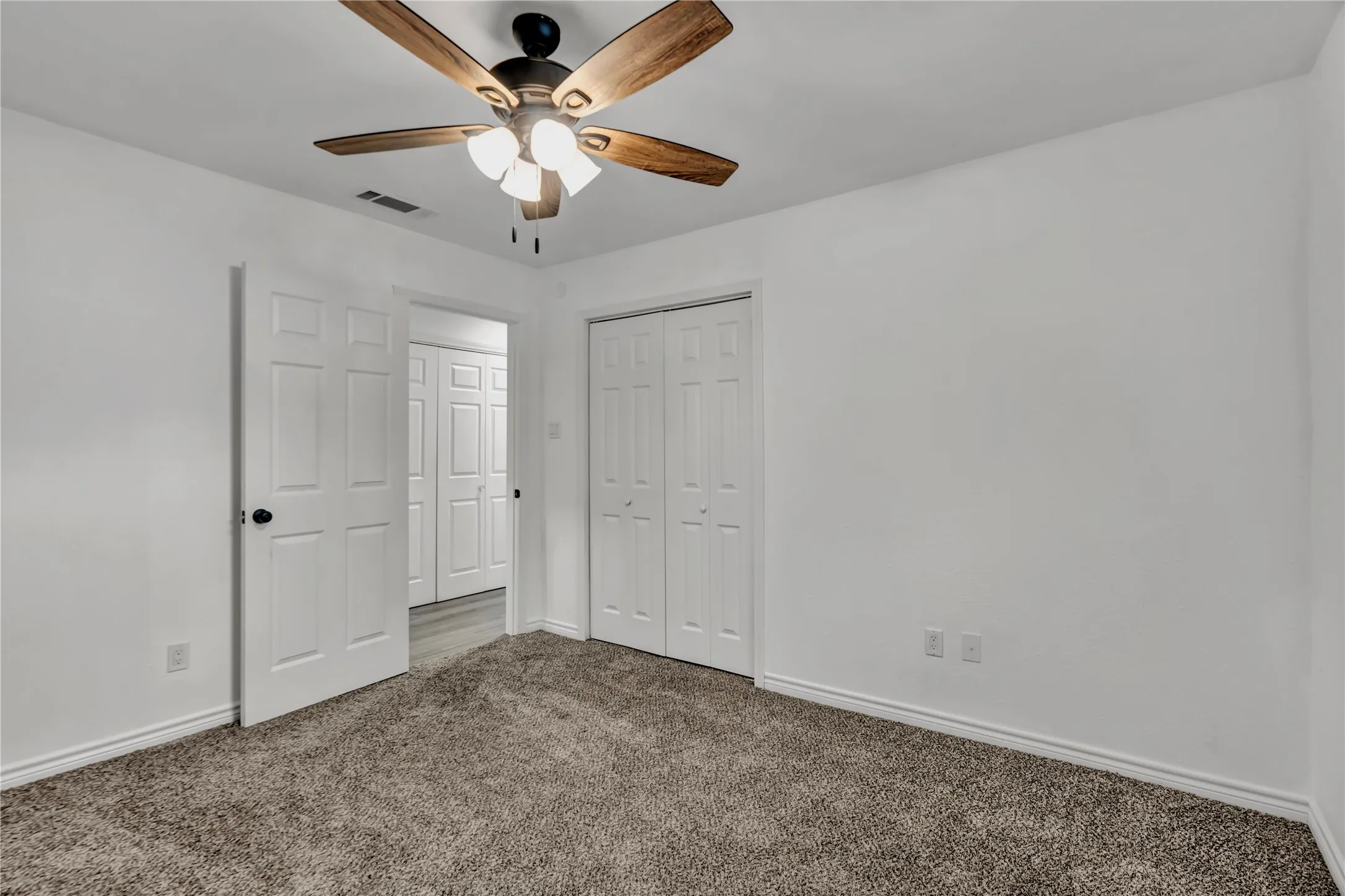 Textured carpet flooring with white baseboards, a ceiling fan with integrated lighting, and a closet with bifold doors