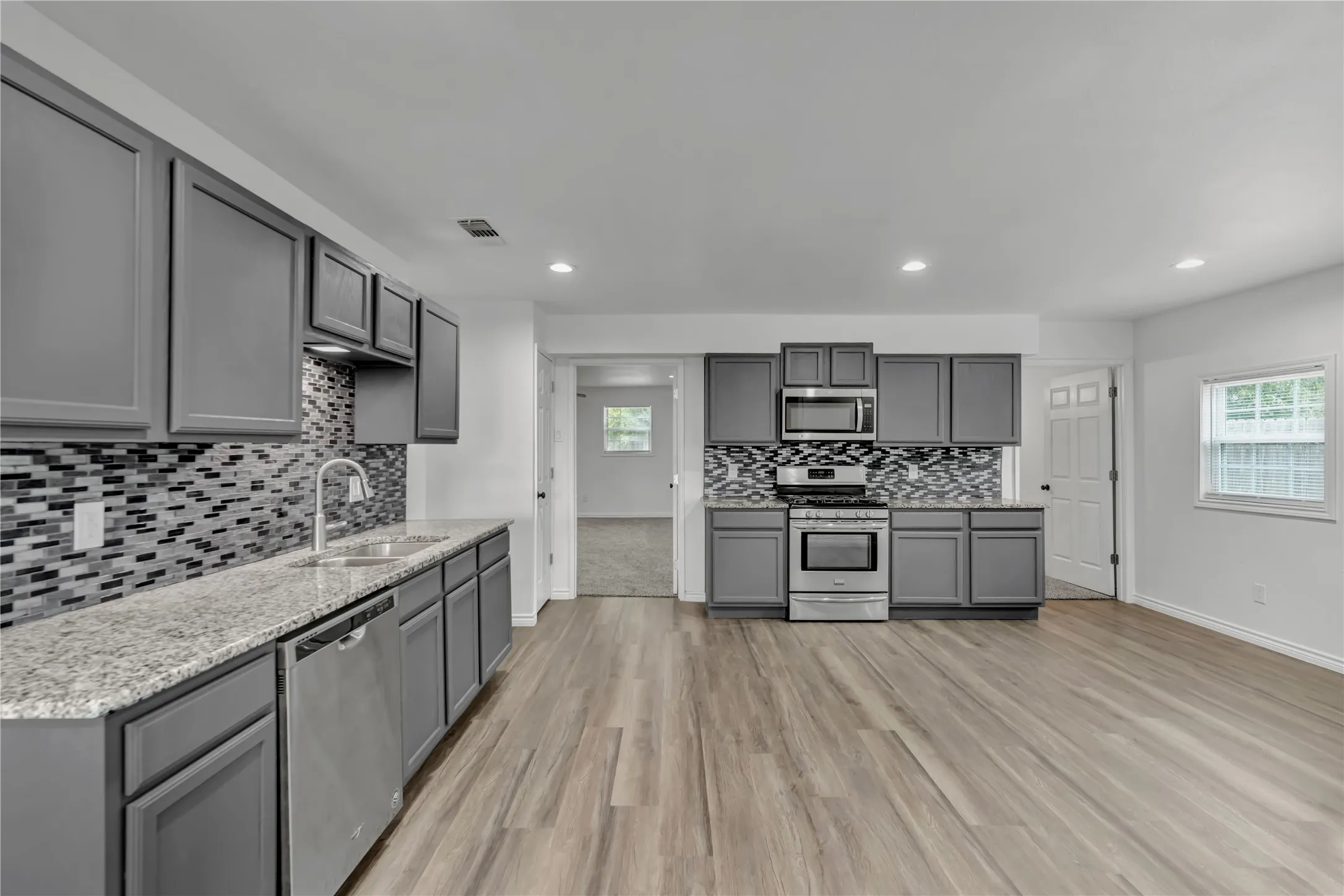 Galley kitchen featuring gray cabinetry, stainless steel appliances, granite-style countertops, and a mosaic tile backsplash