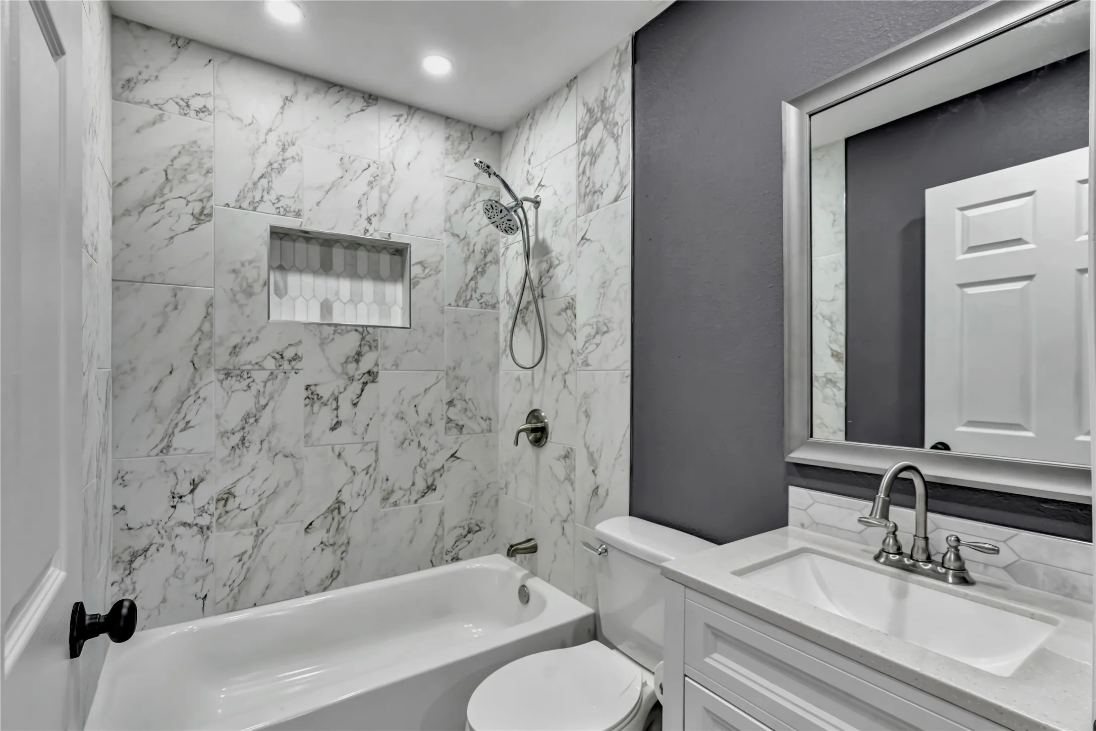 White subway tile bathtub surround with a recessed niche, brushed nickel shower fixtures, and a white vanity with a rectangular sink and brushed nickel faucet