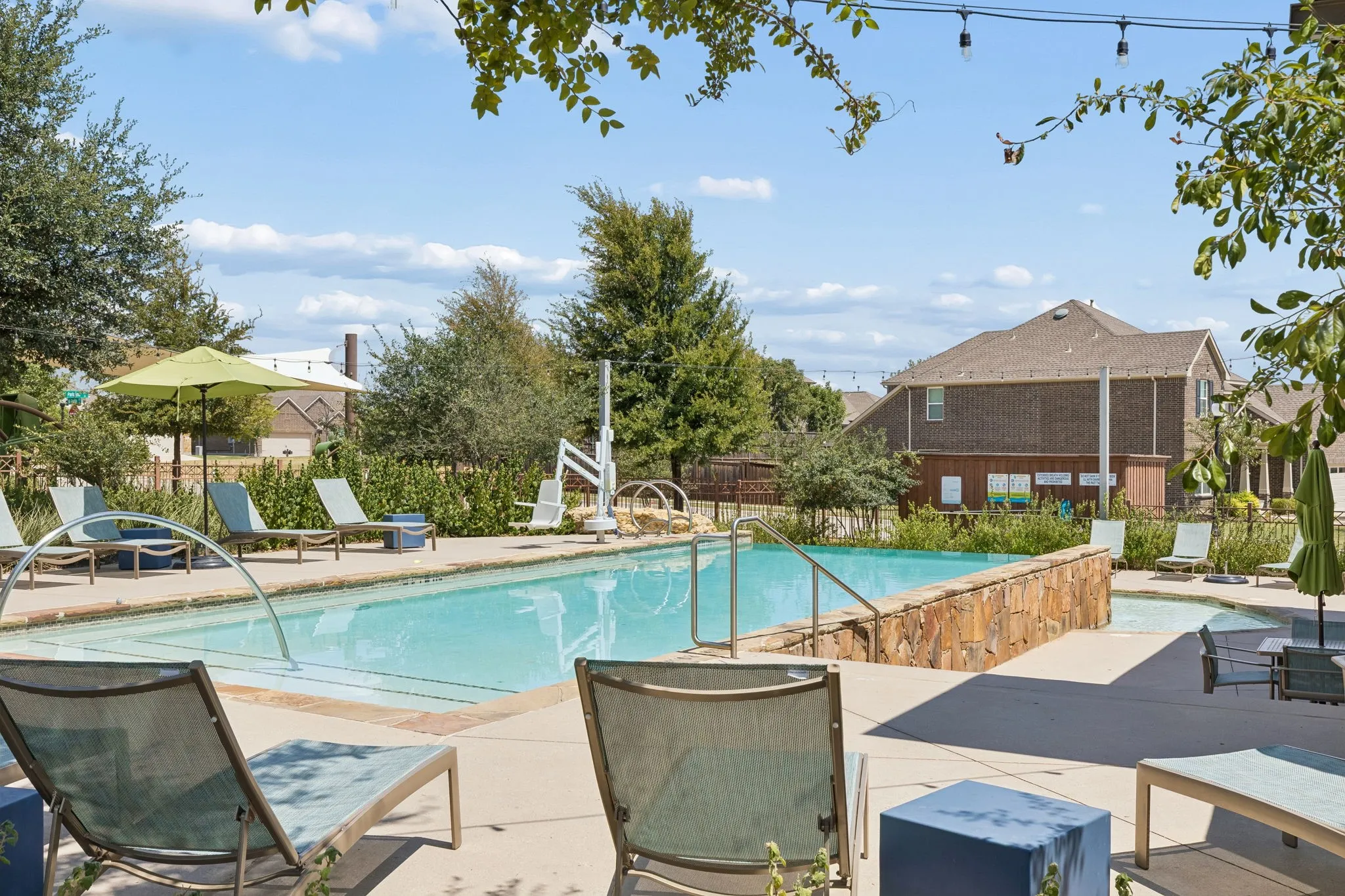 Outdoor swimming pool with integrated spa and stone surround, surrounded by concrete decking and mature landscaping