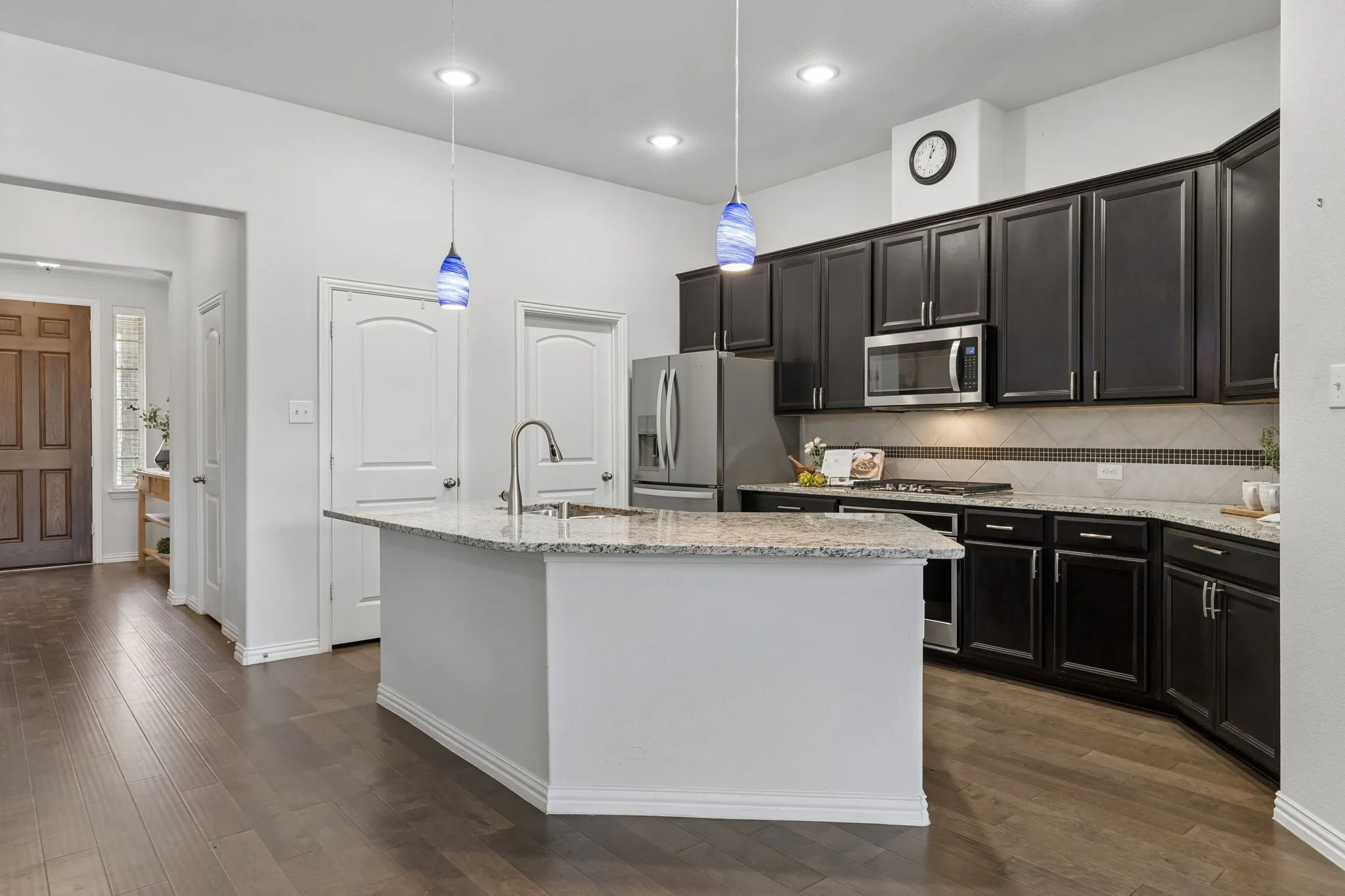 Expansive wood-finish flooring, a kitchen island with a granite countertop, dark wood cabinetry, stainless steel appliances, and recessed lighting