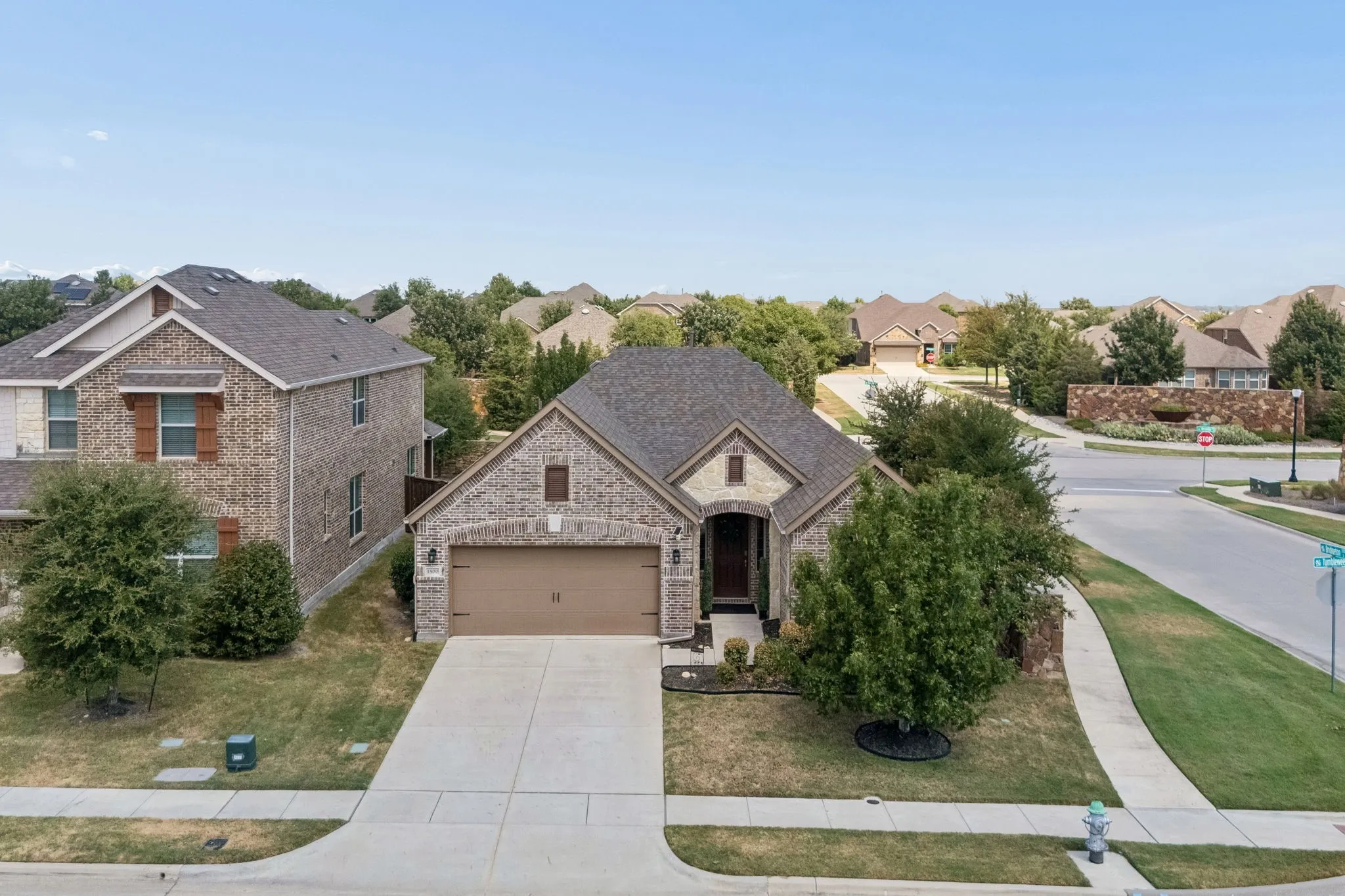 Brick exterior with stone accents, attached garage, concrete driveway, and mature landscaping