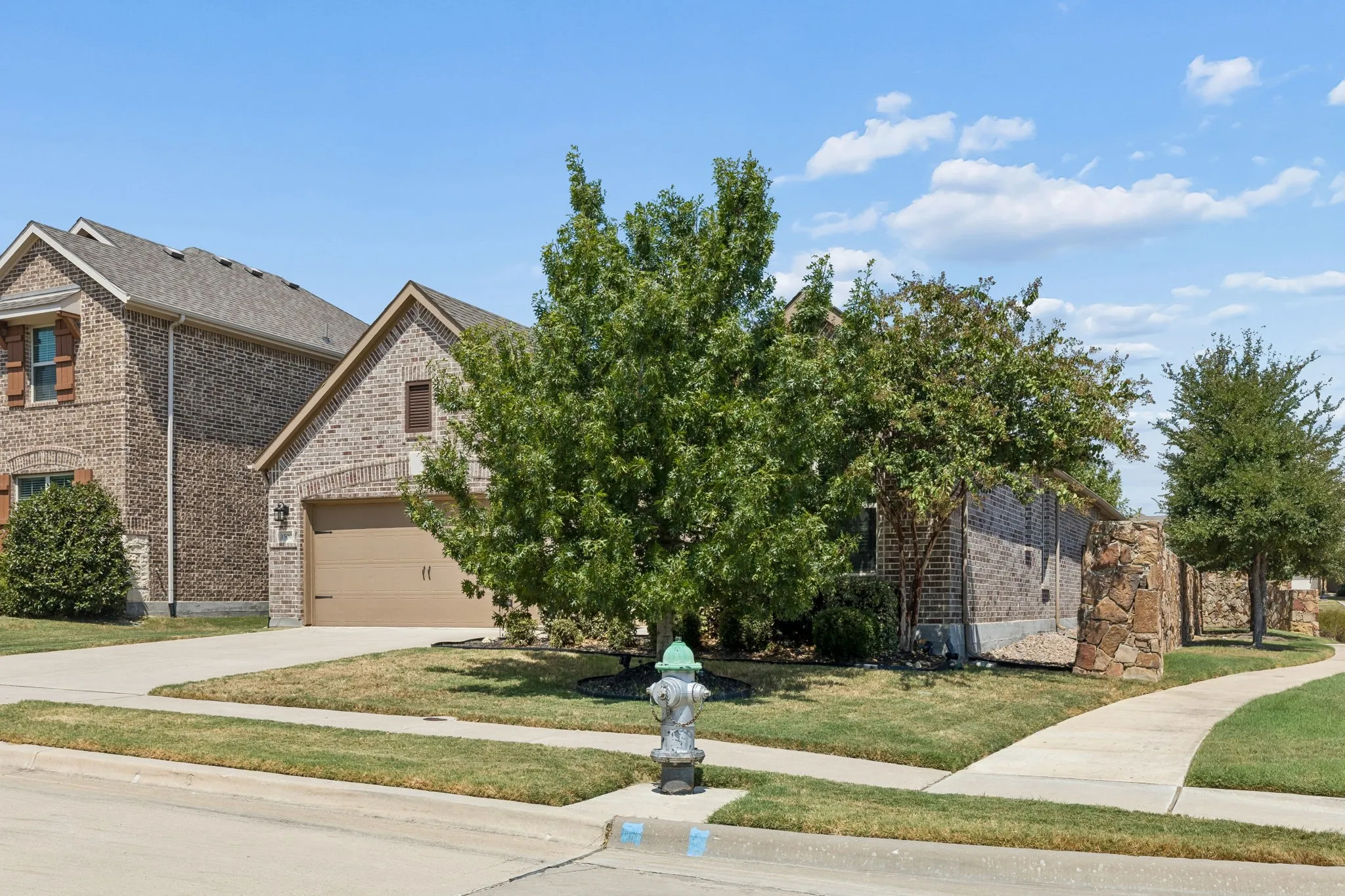 Brick exterior with stone accents, attached garage, concrete driveway, and mature landscaping
