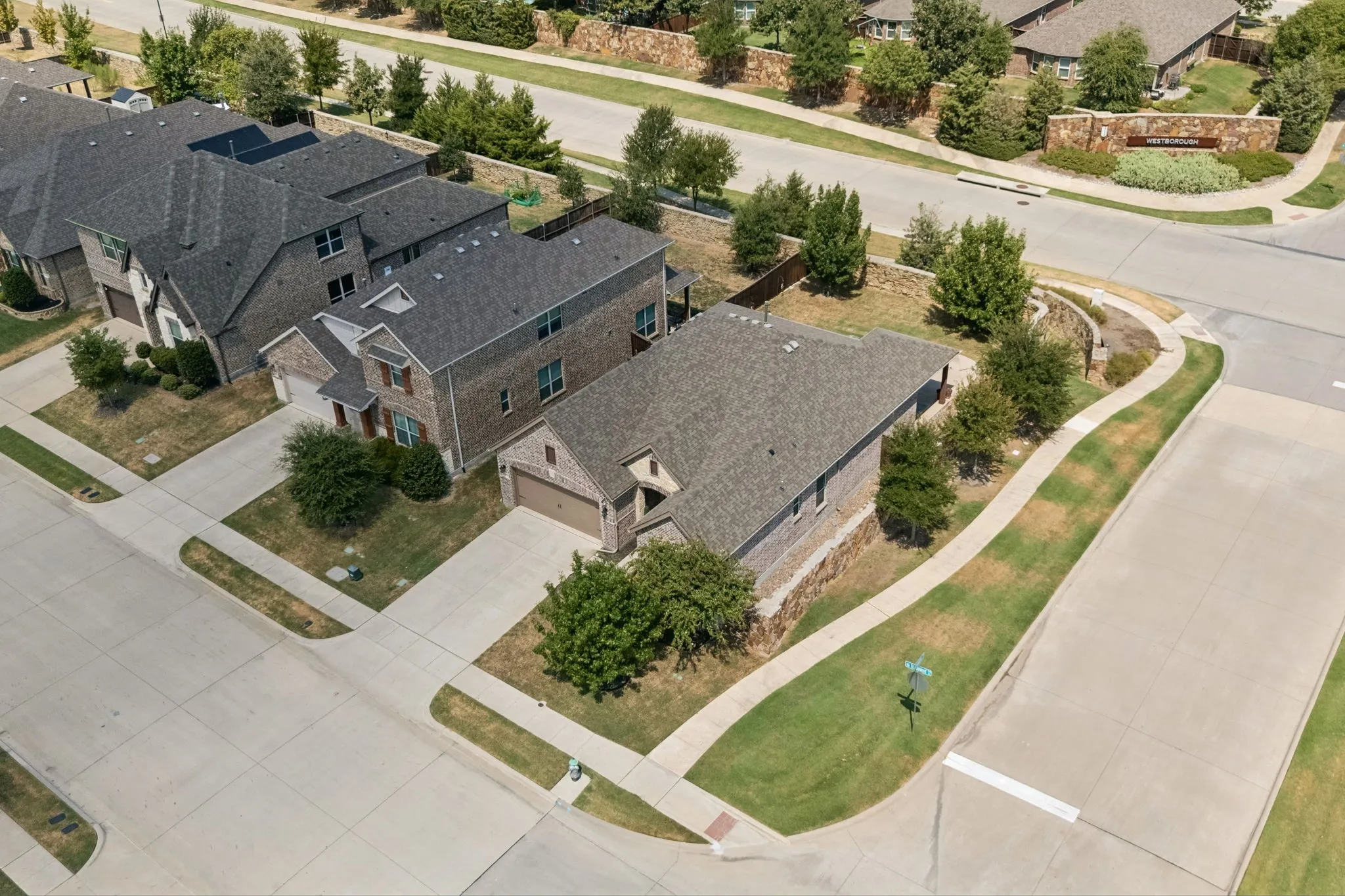 Brick exterior residence with an attached garage, concrete driveway, and mature landscaping
