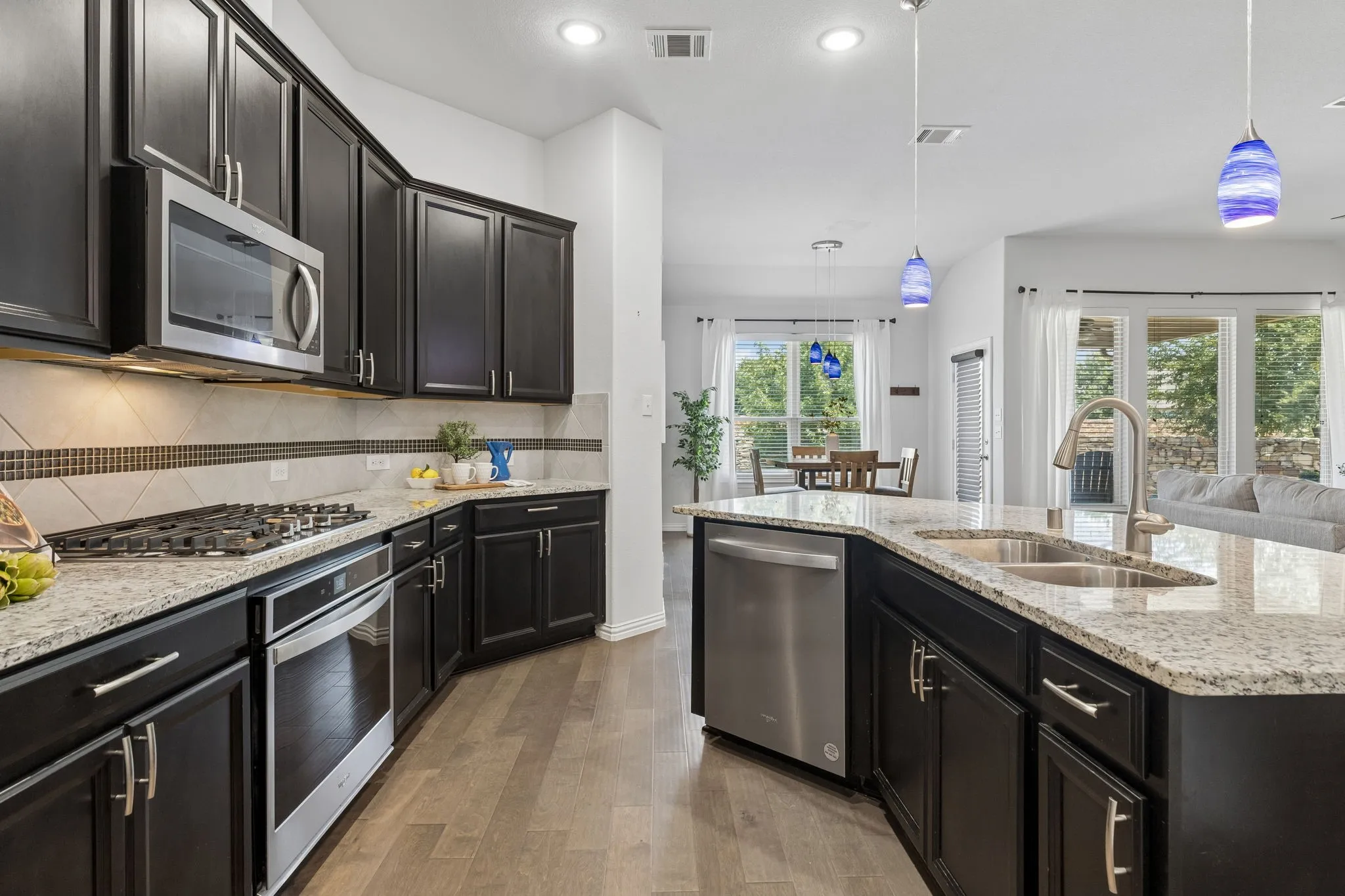 Kitchen featuring dark wood cabinetry, light-toned countertops, stainless steel appliances, and a tile backsplash