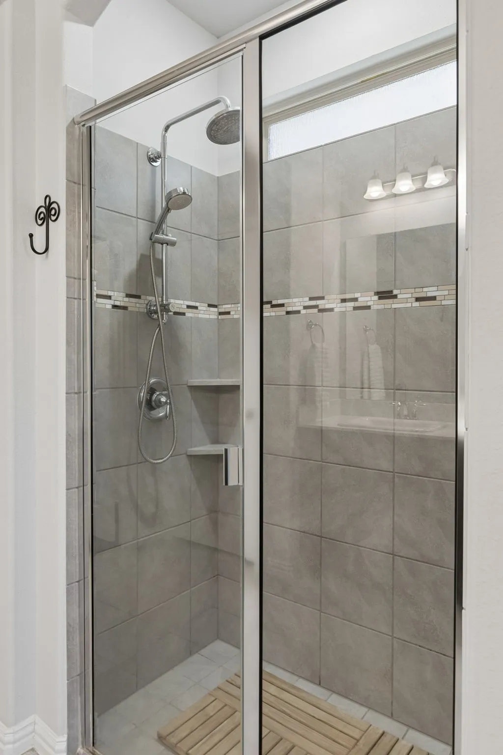 Glass-enclosed shower with a rainfall showerhead, handheld sprayer, integrated shelving, and a decorative tile band