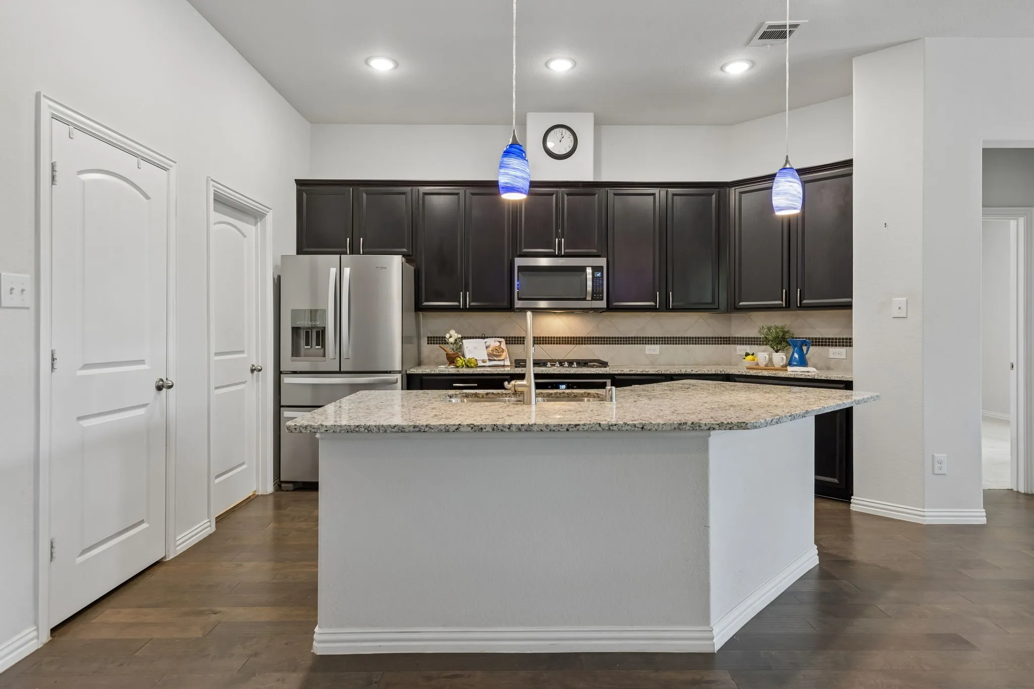 Kitchen featuring dark wood cabinetry, stainless steel appliances, a center island with light speckled countertops, and wood-finish flooring