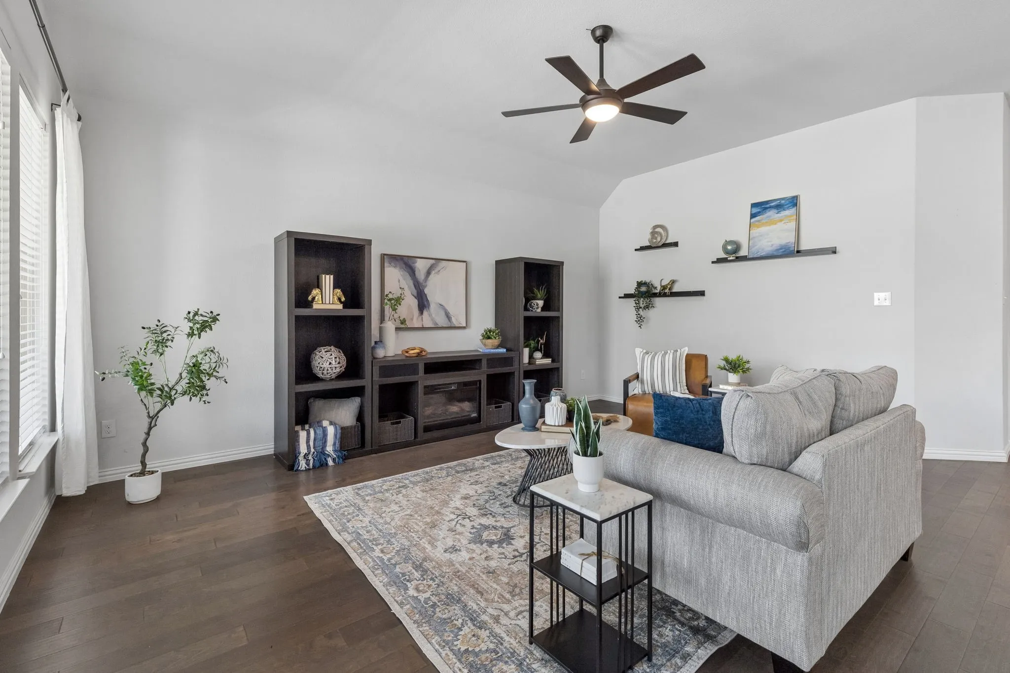Vaulted ceiling with a ceiling fan, wood-finish flooring, white walls, built-in shelving, and large windows