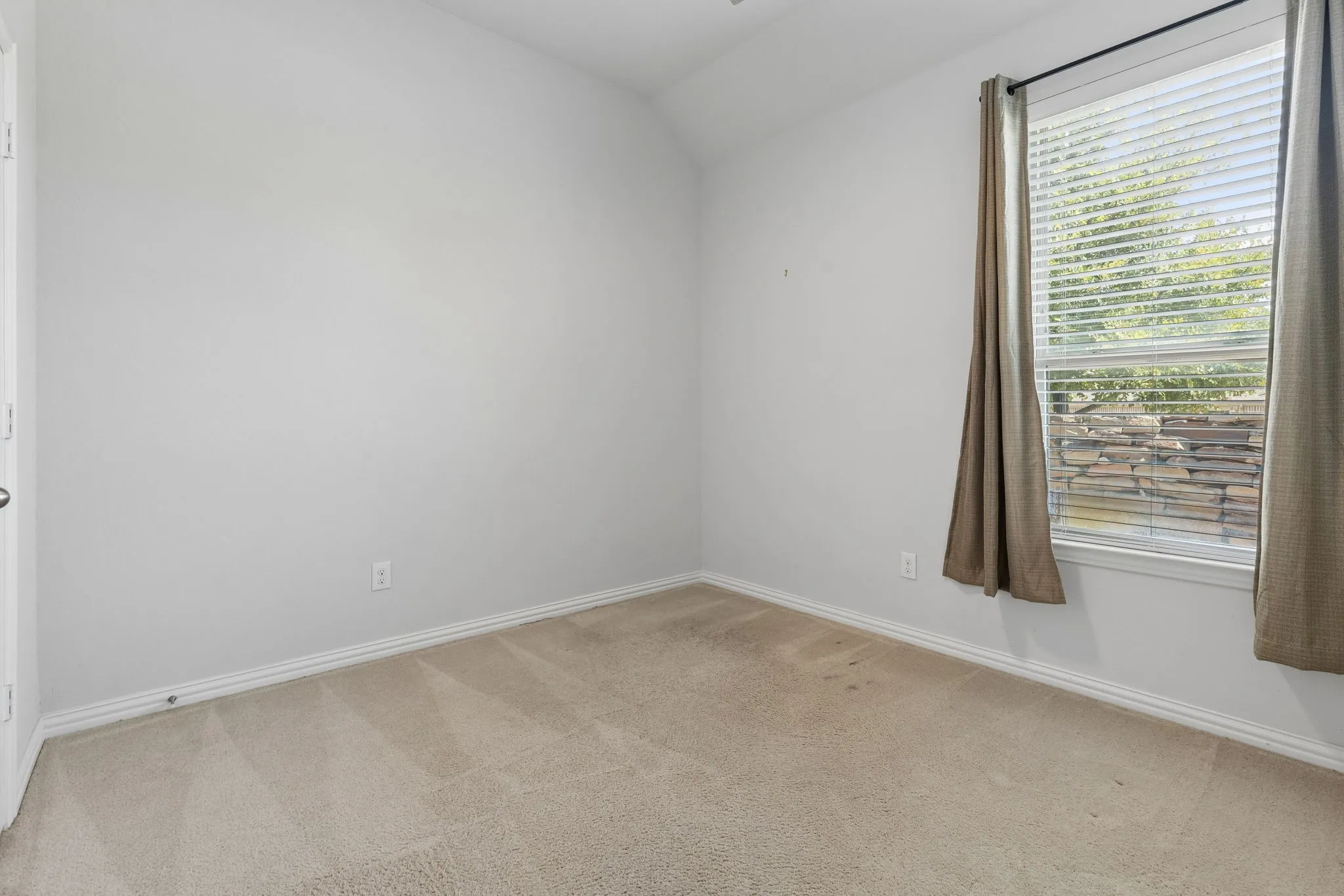 Carpeted room with a vaulted ceiling and a single window