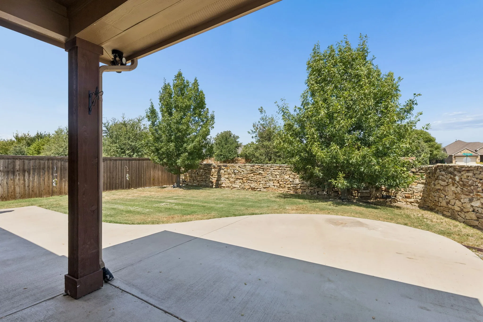 Covered patio with a concrete surface, expansive lawn, stone wall, and wood fence