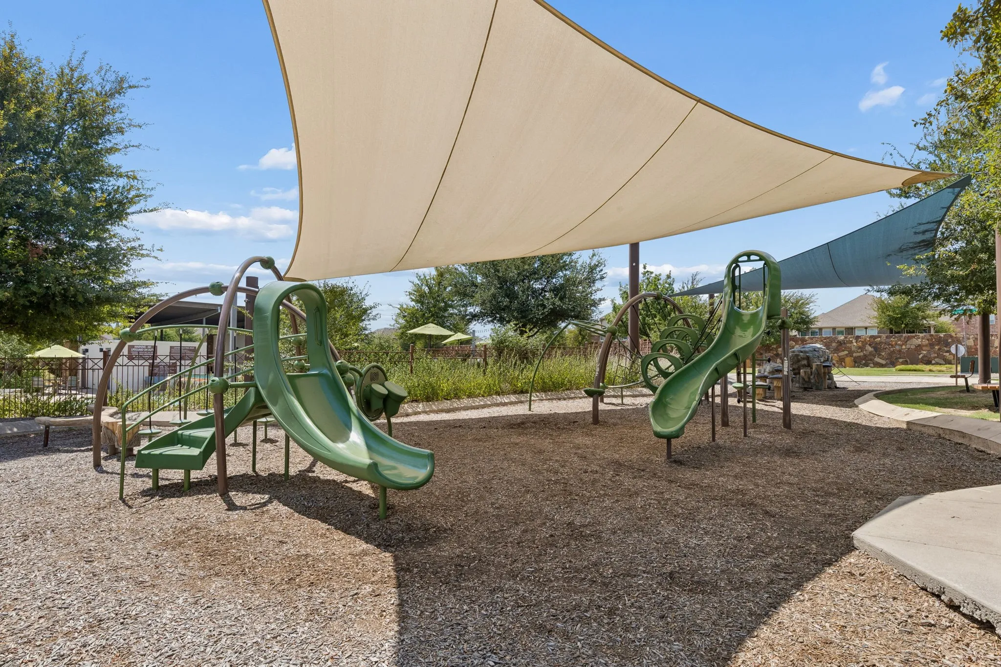 Playground featuring two green slides, climbing elements, and a protective shade canopy