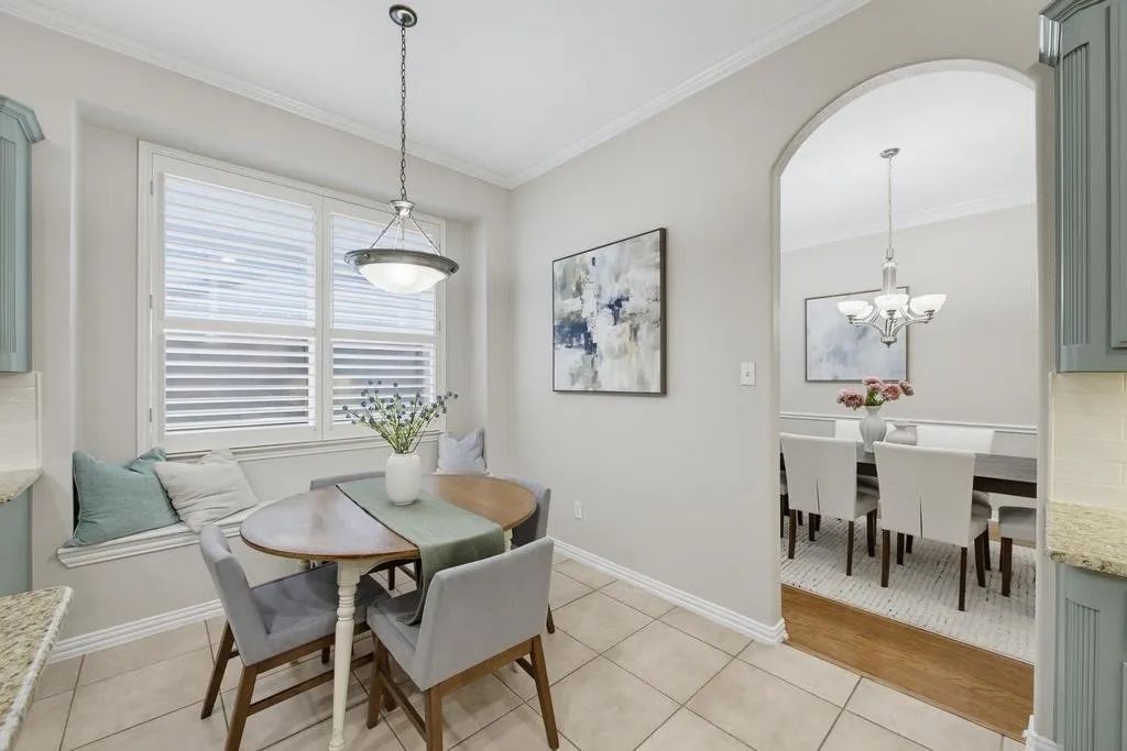 Built-in window bench seating with plantation shutters, tile flooring, and an arched doorway leading to an additional dining area