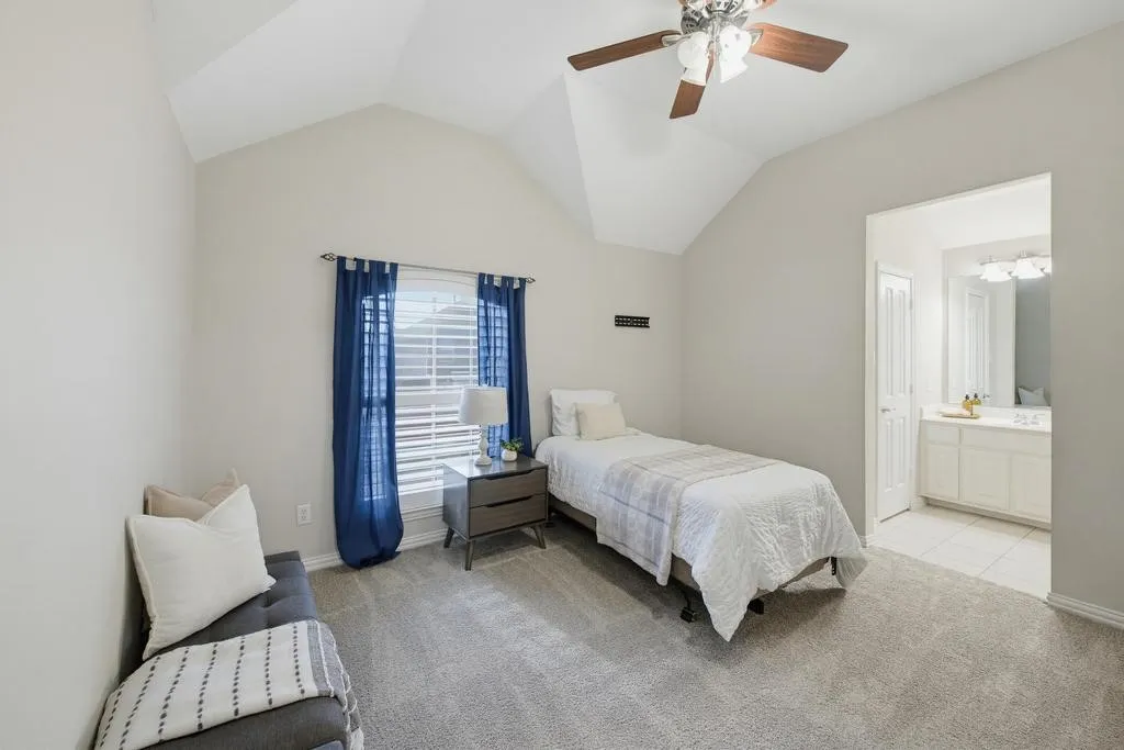 Vaulted ceiling, ceiling fan, carpeted flooring, window with blinds, and an attached vanity with integrated sink