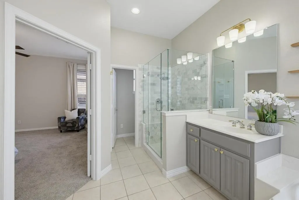 Dual sink vanity with grey cabinetry and light countertop, glass-enclosed shower with tiled surround, and tiled flooring