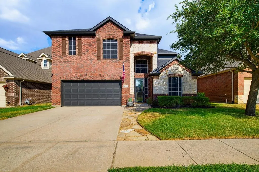 Brick and stone-veneer exterior with a two-car garage, mature landscaping, and a stone pathway