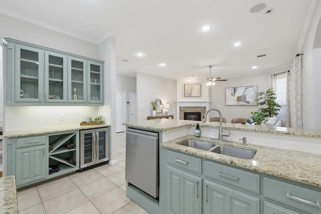 Kitchen featuring light-toned cabinetry, granite countertops, stainless steel dual basin sink, tile flooring, and integrated wine refrigeration