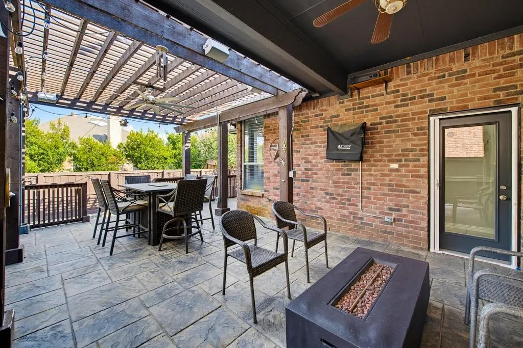 Outdoor patio featuring a wooden pergola, ceiling fan, brick exterior wall, glass-paneled door, and stamped concrete flooring