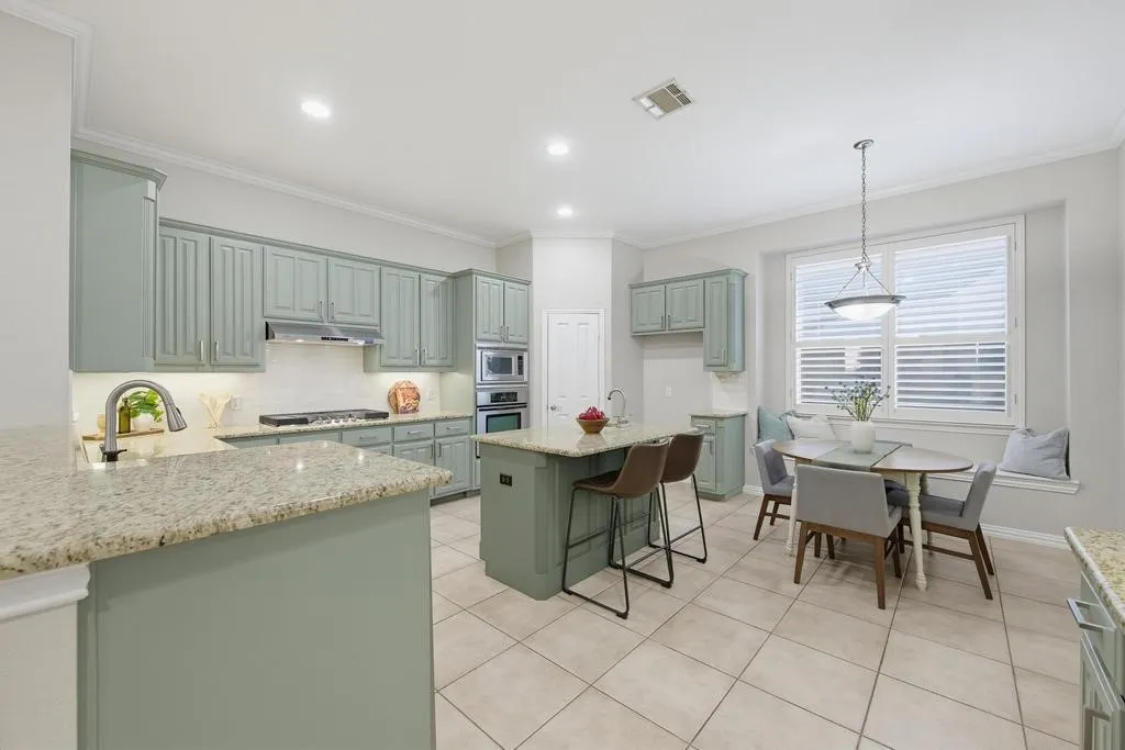 Kitchen featuring light green cabinetry, granite countertops, stainless steel appliances, a center island with seating, and tile flooring